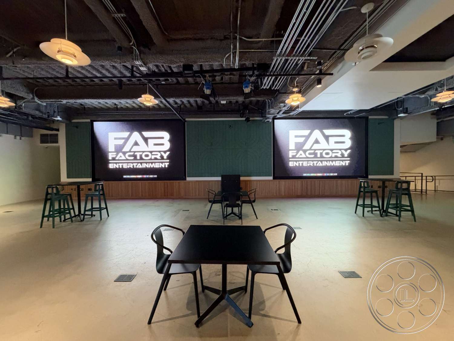 Office 130 - exterior, concrete flooring, modern pendant lighting, urban setting, metal bar stools, rectangular table, large digital display screen, wood panel accent wall, exposed ductwork ceiling, open entertainment space