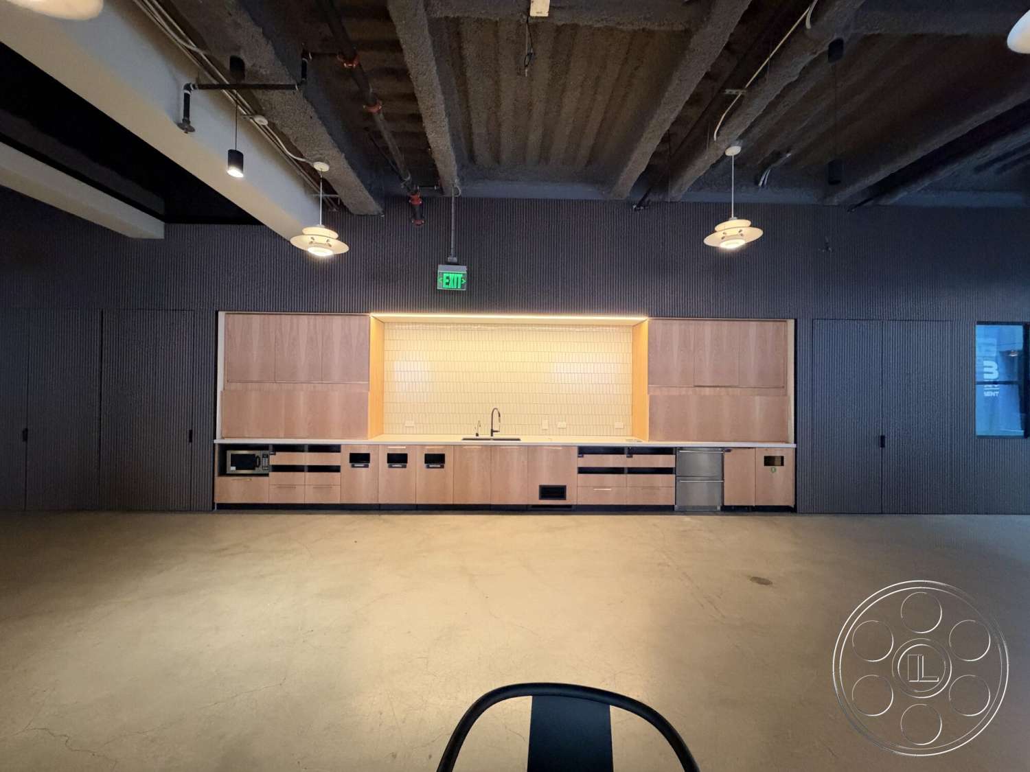 Office 130 - open floor plan, stainless steel appliances, floor-to-ceiling windows, minimalist kitchen design, white subway tile backsplash, exposed concrete flooring, linear lighting fixtures, modern industrial style, wood kitchen cabinets, textured ceiling paneling, black ribbed wall panels
