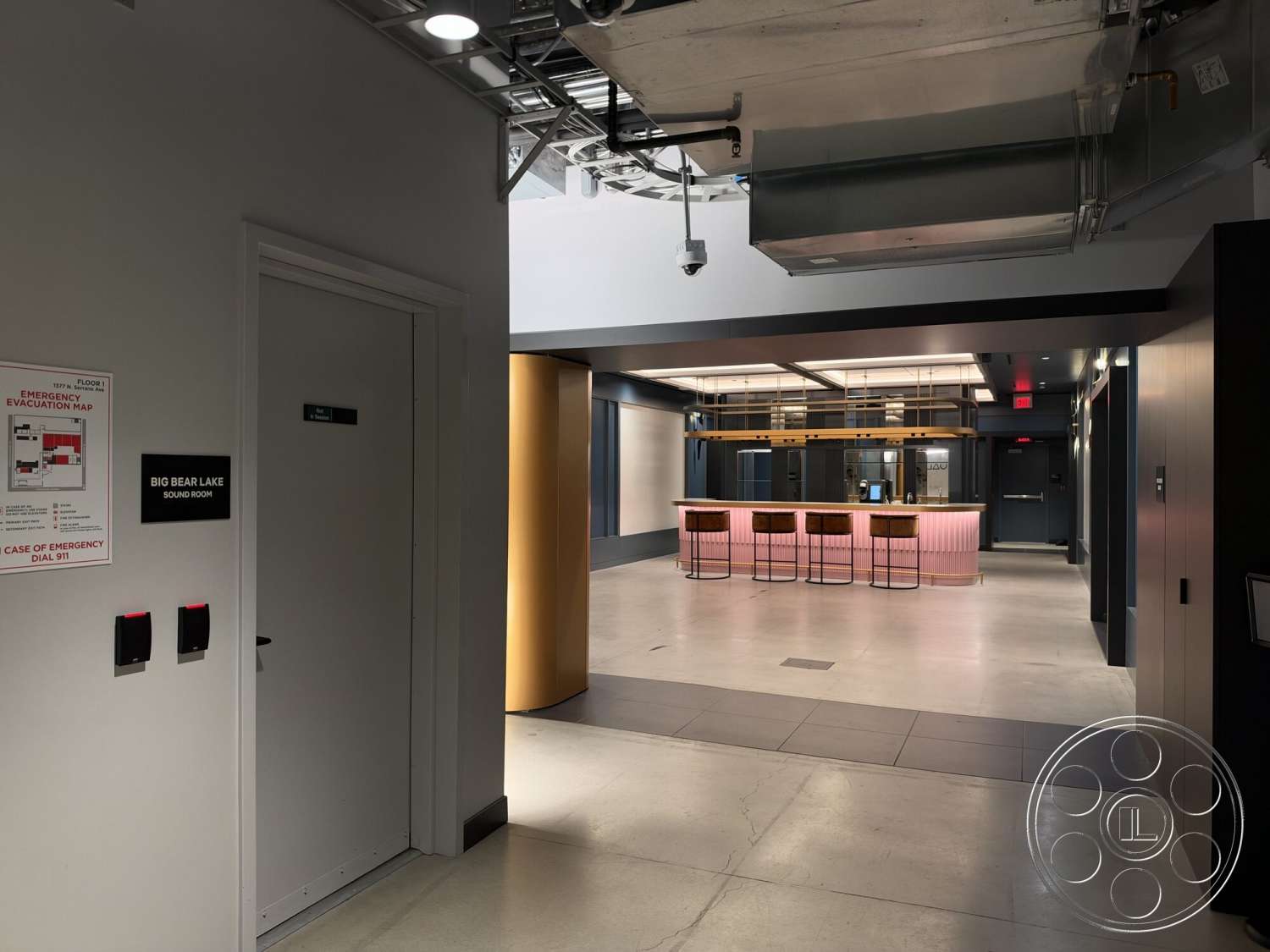 Office 130 - multifunctional space, concrete flooring, exposed ductwork, textured wall treatments, wood bar stools, modern bar area, metal pendant lighting, painted drywall walls, integrated lighting fixtures, open layout design, glass door entrance, colorful backlit bar