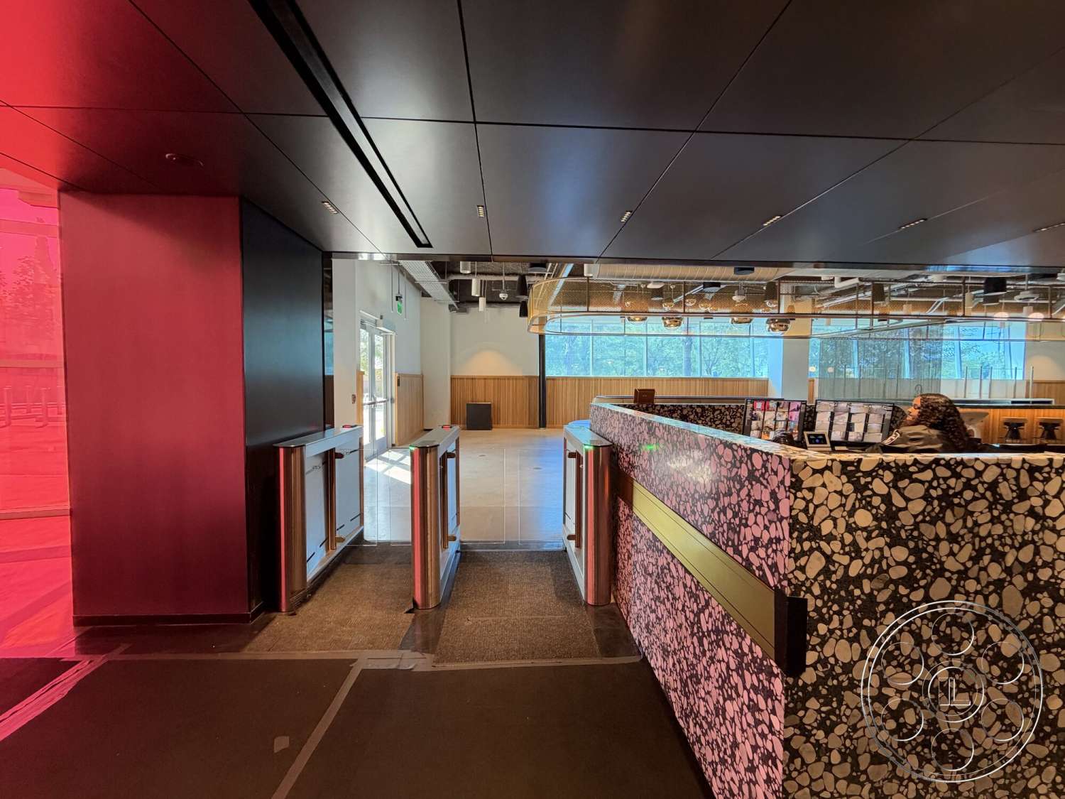 Office 130 - polished concrete flooring, modern lighting fixtures, minimalist design elements, floor-to-ceiling windows, open office layout, wood paneling wall treatment, black acoustic ceiling panels, multi-functional workspace, natural light utilization, terrazzo reception desk, stainless steel entrance gates