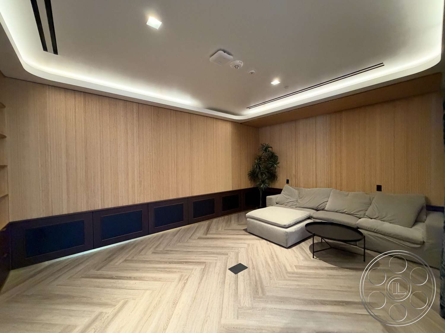 Office 130 - neutral color palette, round coffee table, modern aesthetic, floor-to-ceiling windows, low-profile sectional sofa, recessed ceiling lighting, herringbone patterned wood flooring, wood panel wall treatment