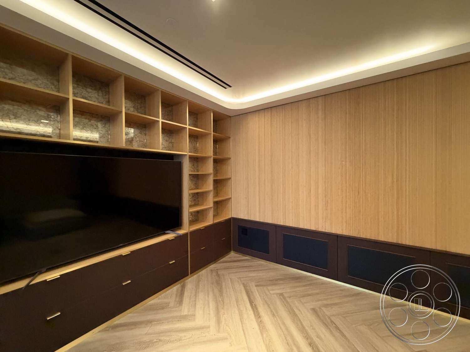Office 130 - dark wood cabinetry, herringbone wood flooring, recessed ceiling lighting, modern minimalist design, textured wood panel wall, open shelving with marble backing, black TV stand
