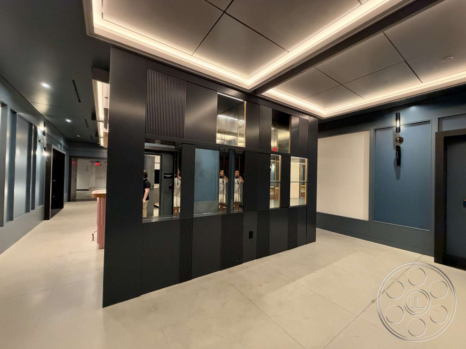 Office 130 - open layout, concrete floor, textured accent wall, industrial style, vaulted ceiling, neutral color scheme, cohesive color palette, linear lighting fixtures, modern ceiling design, glass window panels, black wall treatments, mirror accents, sleek furniture elements