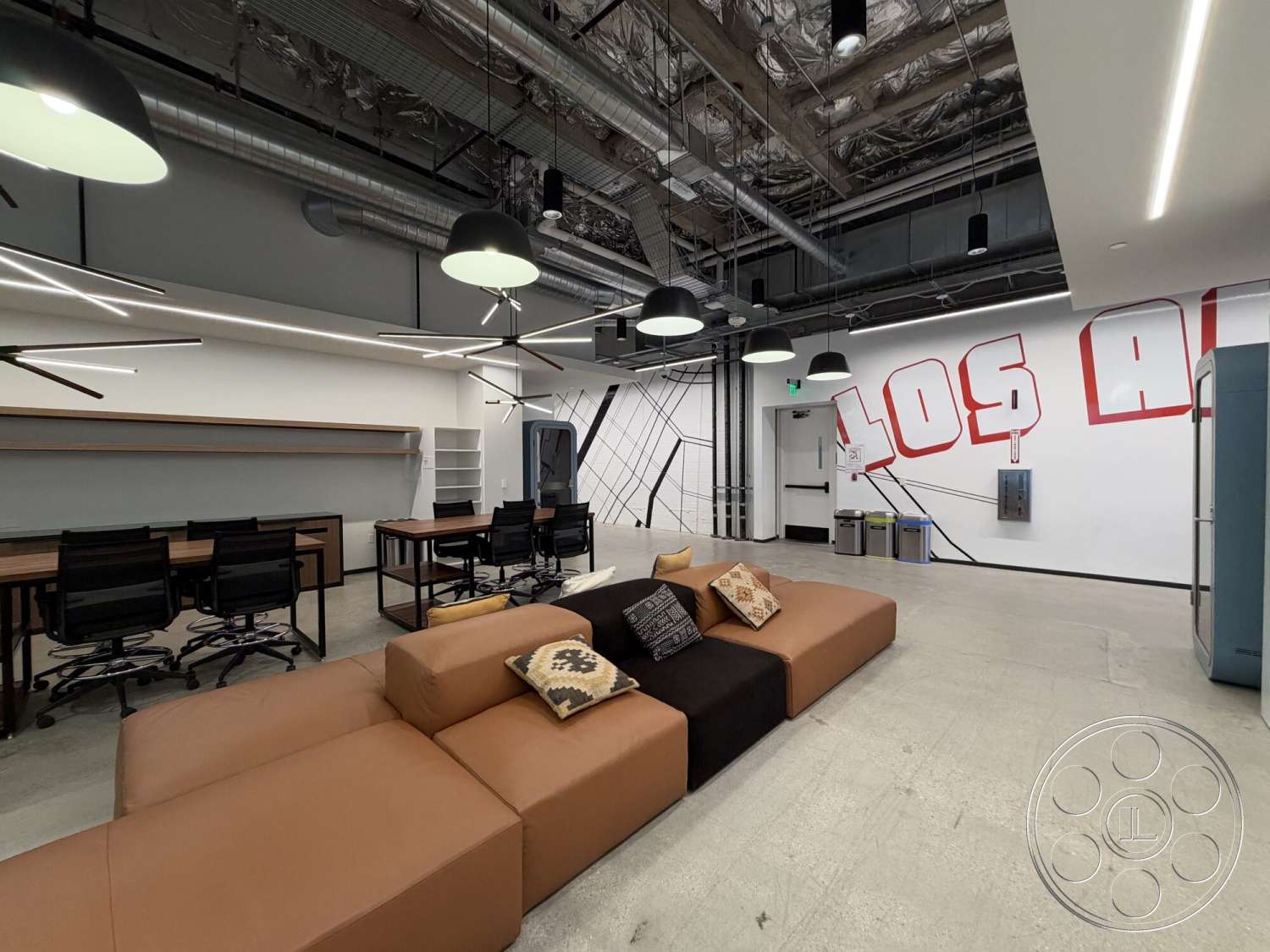 Office 130 - large windows, floating shelves, concrete flooring, creative environment, functional workspace, exposed ductwork, open office layout, brown leather sectional sofa, white painted walls, modern office desks, black ergonomic office chairs, industrial ceiling lights, graphic wall mural