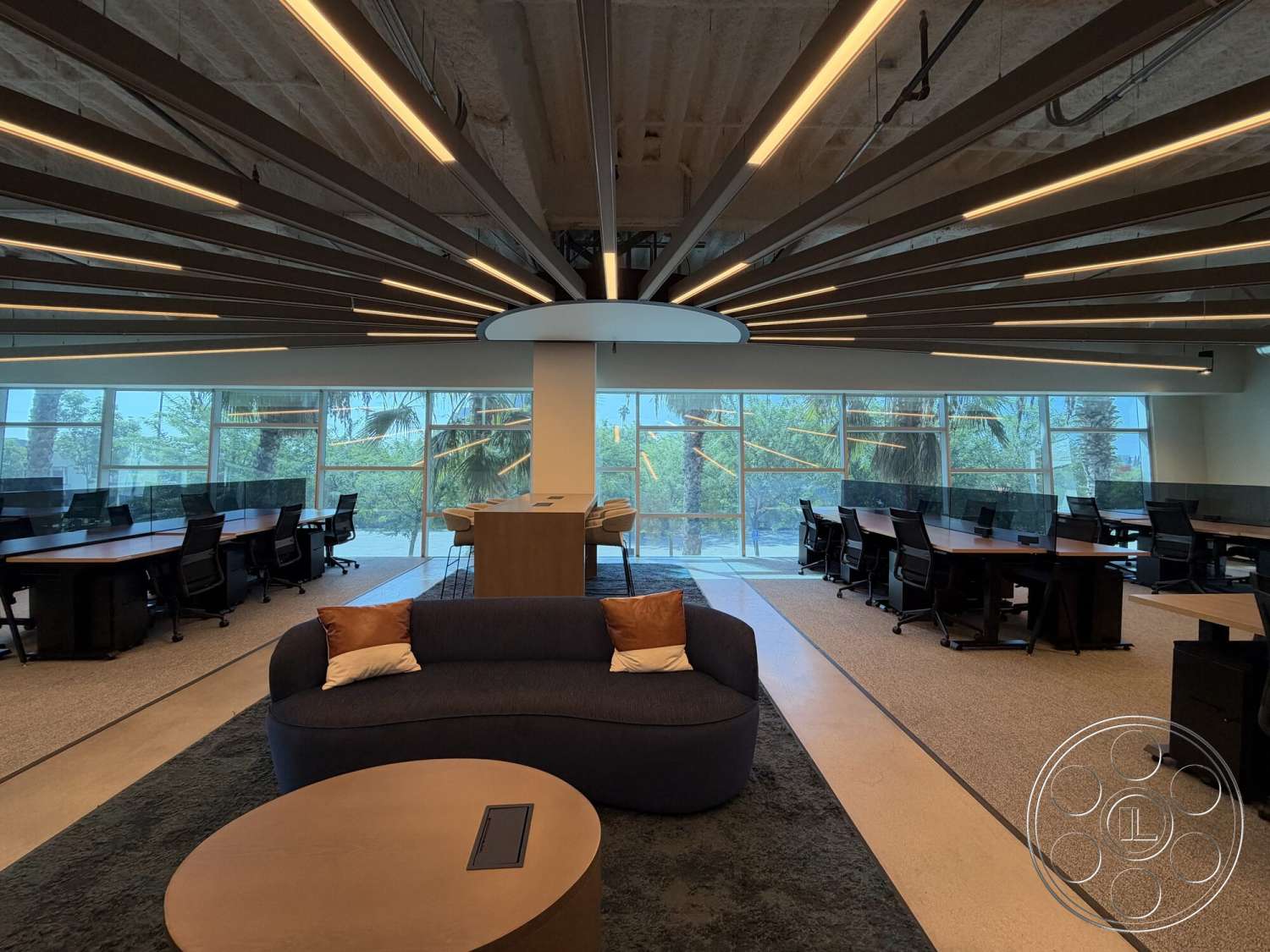 Office 130 - concrete flooring, greenery view, large floor-to-ceiling windows, round wooden coffee table, glass partition walls, textured carpet area, industrial style architecture, open workspace layout, interior modern office, suspended ceiling with linear LED lighting, dark wood conference tables, metal framed office chairs, curved blue lounge sofa