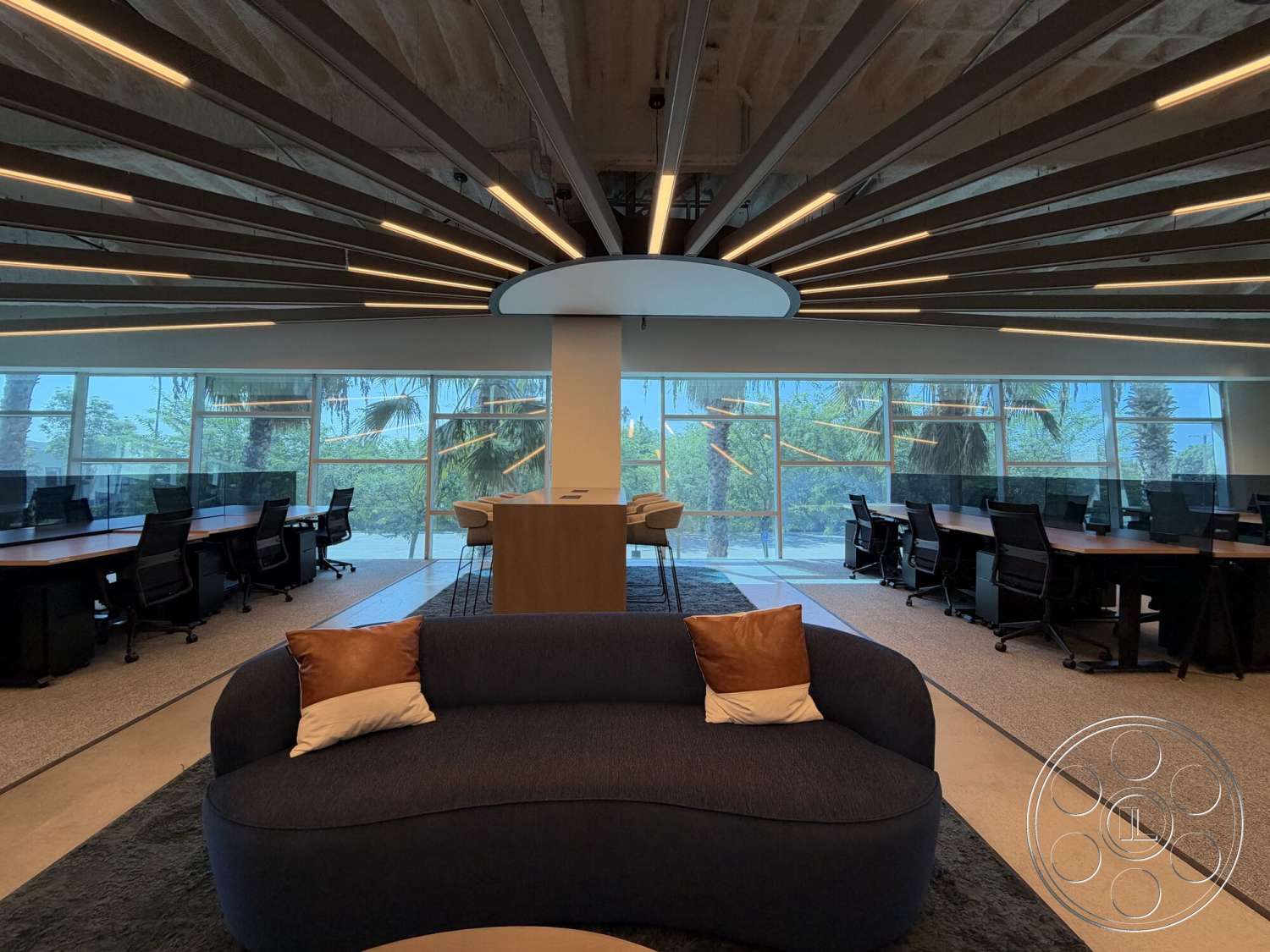 Office 130 - polished concrete floor, minimalist design elements, gray carpet flooring, open office layout, glass wall partitions, ergonomic office chairs, exposed wood ceiling beams, natural light flooding the space, recessed LED lighting, modern office furniture, rectangular conference table, curved sofa with decorative pillows, large windows with palm view