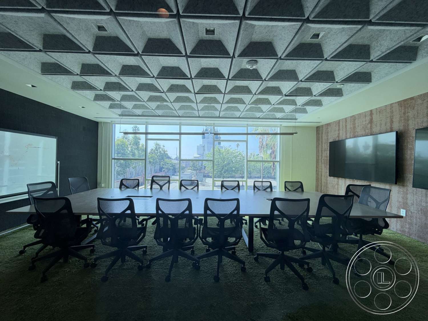 Office 130 - carpet flooring, wood conference table, whiteboard wall, acoustic panel ceiling, rolling office chairs, glass conference room windows, hexagonal ceiling tiles, dark fabric wall treatment, multiple wall-mounted televisions
