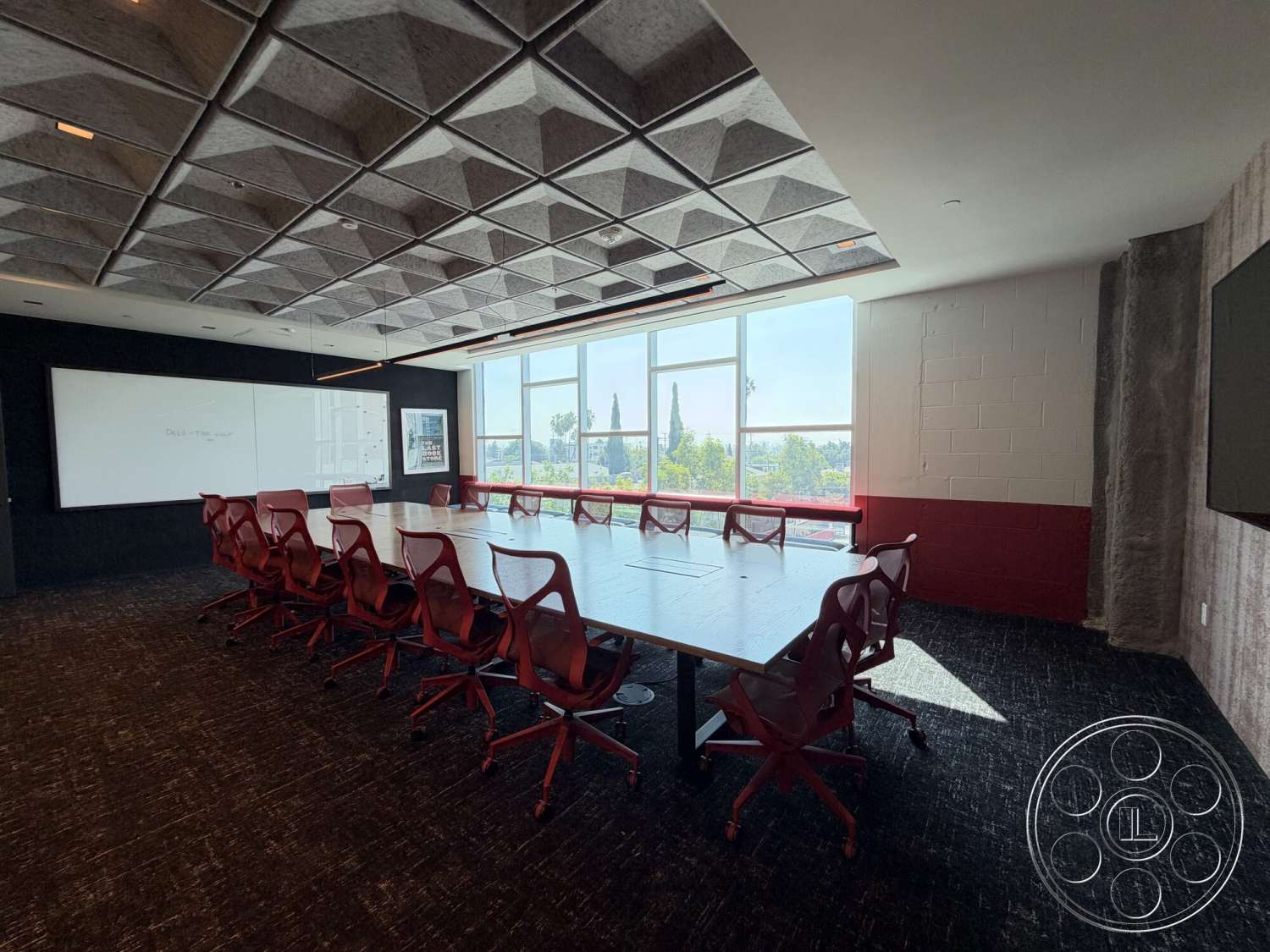 Office 130 - modern lighting fixtures, black accent wall, interior conference room, textured ceiling tiles, dark carpet flooring, glass windows with city view, wood conference table, whiteboard wall, red swivel chairs, exposed concrete wall section