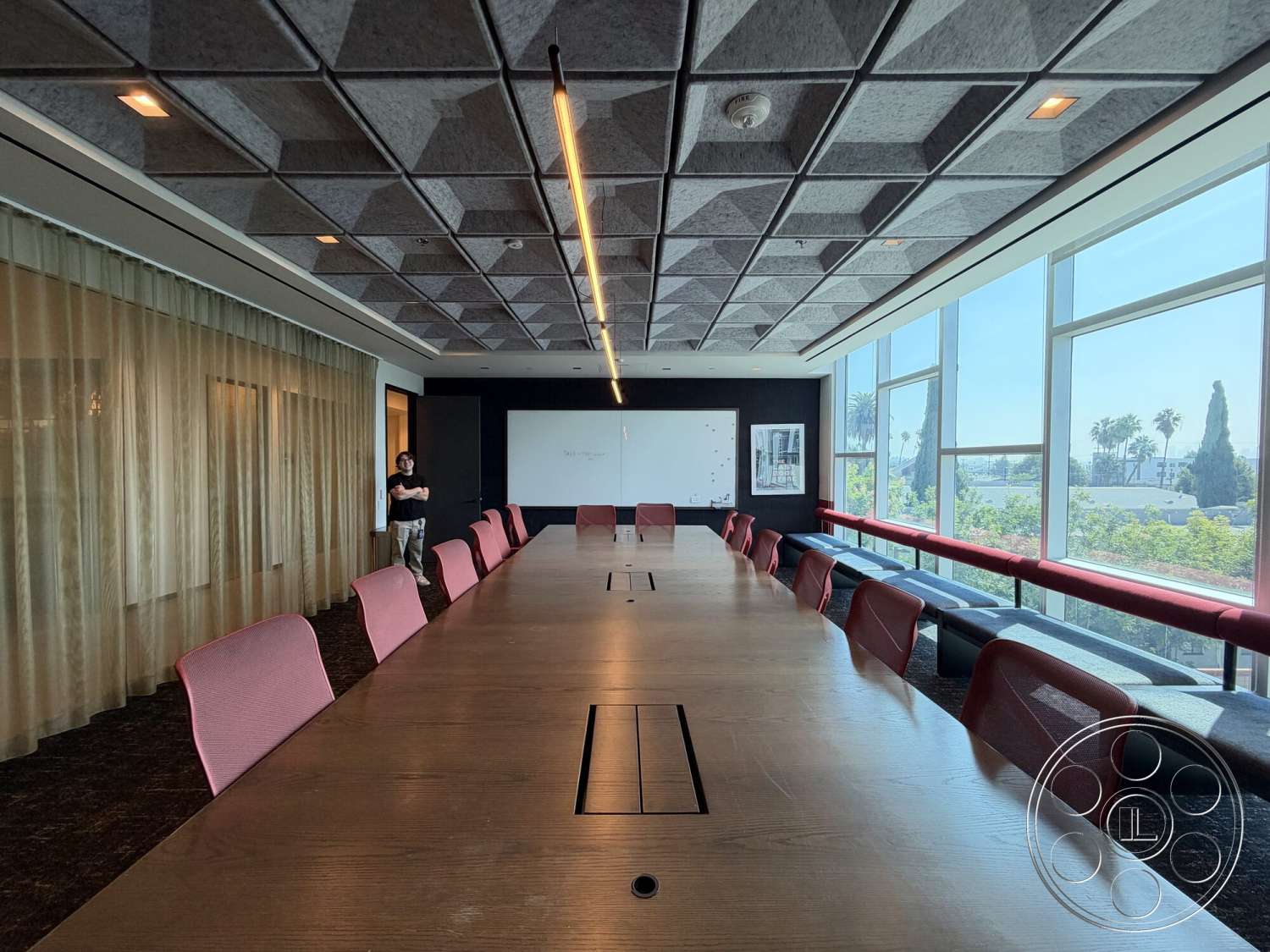 Office 130 - floor-to-ceiling windows, glass wall panels, modern meeting space, long wooden conference table, geometric acoustic ceiling tiles, rose-colored ergonomic seating, light wood table finish, black floor tiles, soft fabric curtain divider