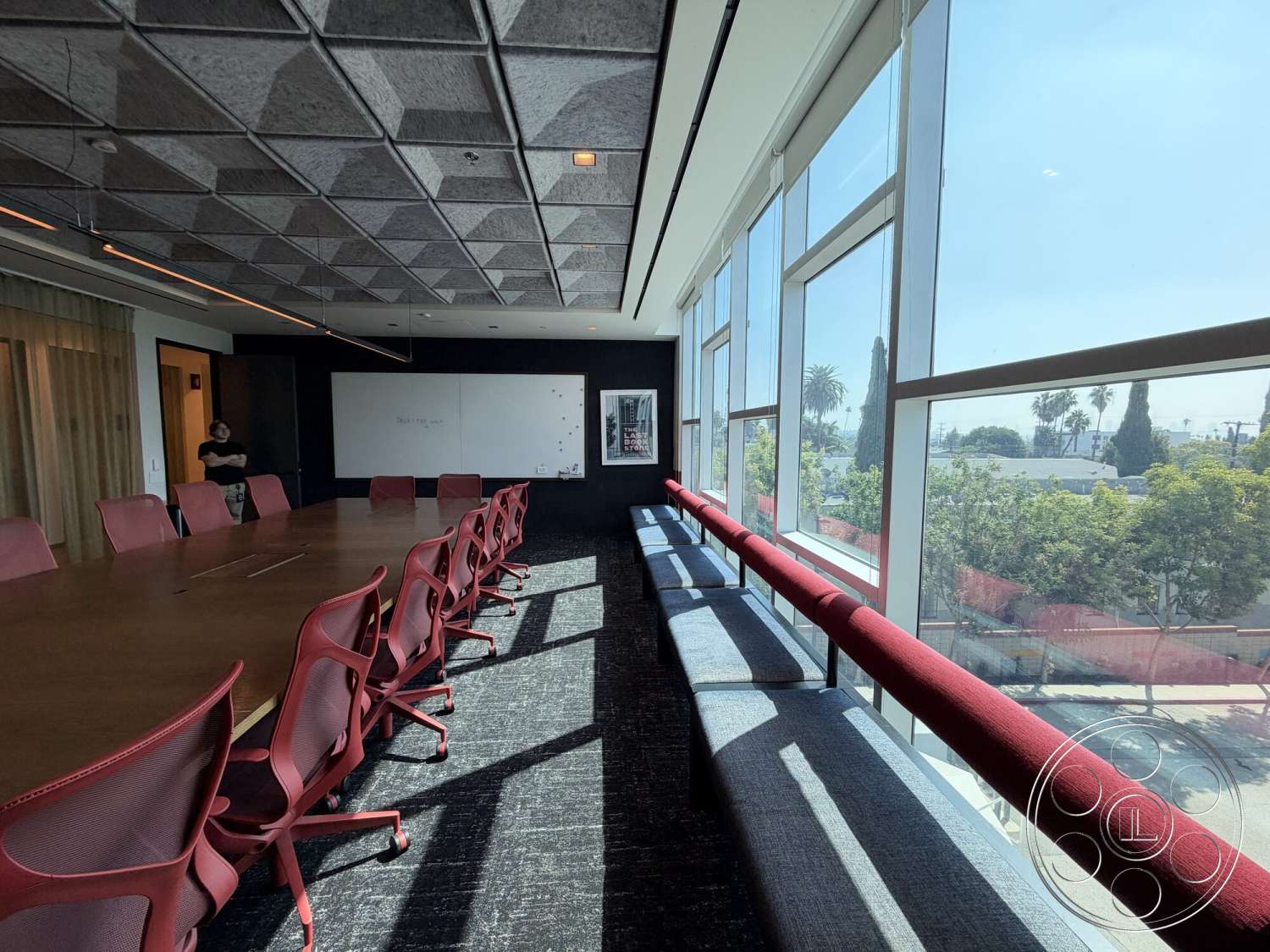 Office 130 - large floor-to-ceiling windows, black accent wall, gray carpet flooring, acoustic ceiling tiles, modern office design, wood conference table, whiteboard wall, bold red office chairs, window bench seating with red cushion