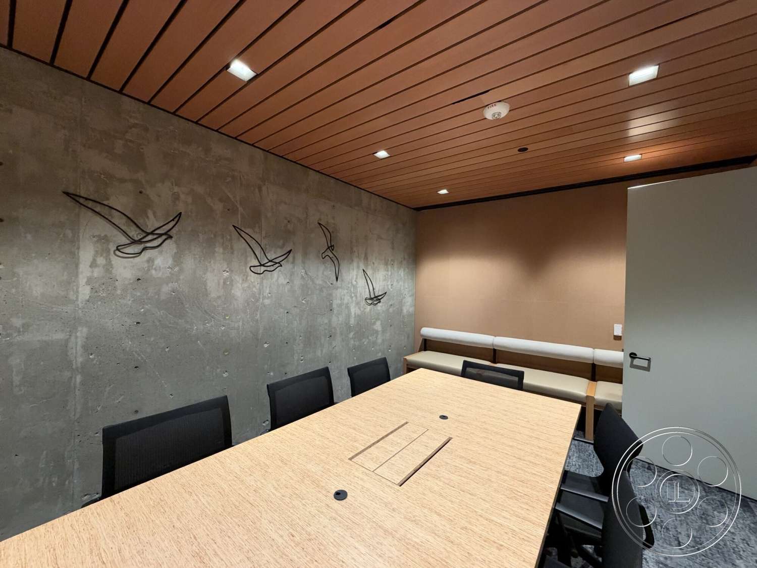 Office 130 - wood ceiling panels, gray carpet flooring, minimalist wall art, concrete feature wall, recessed LED lighting, rectangular conference table, acoustic wall treatment, black mesh office chairs, beige upholstered bench seating