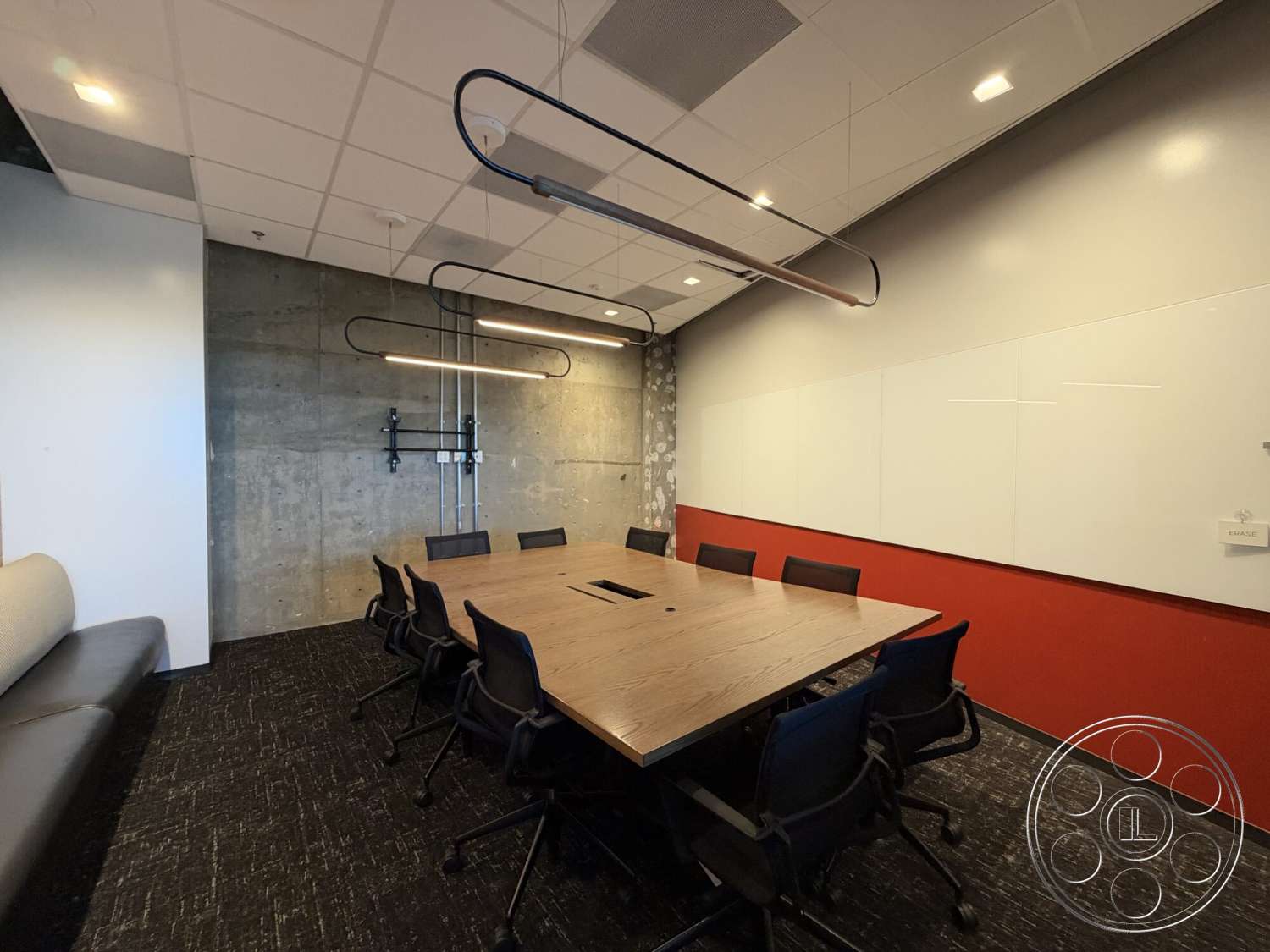 Office 130 - exposed concrete wall, red accent wall, linear pendant lighting, black office chairs, acoustic ceiling tiles, textured carpet flooring, wood conference table, whiteboard wall, metal wall-mounted fixtures