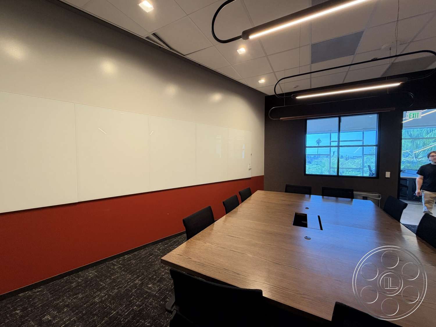 Office 130 - floor-to-ceiling windows, red accent wall, recessed ceiling lights, textured carpet flooring, interior conference room, linear lighting fixtures, wood conference table, modern office decor, whiteboard wall panels, black upholstered office chairs