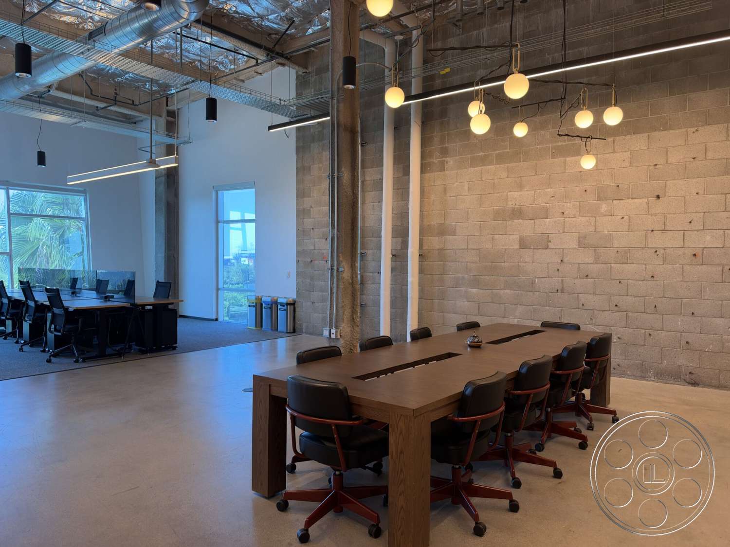 Office 130 - minimalist aesthetic, open layout, large glass windows, concrete floors, collaborative workspace, pendant lighting fixtures, modern office design, workspace with natural light, wood conference table, black ergonomic office chairs, exposed concrete block walls, metal ceiling beams, strategic lighting design, overhead ductwork