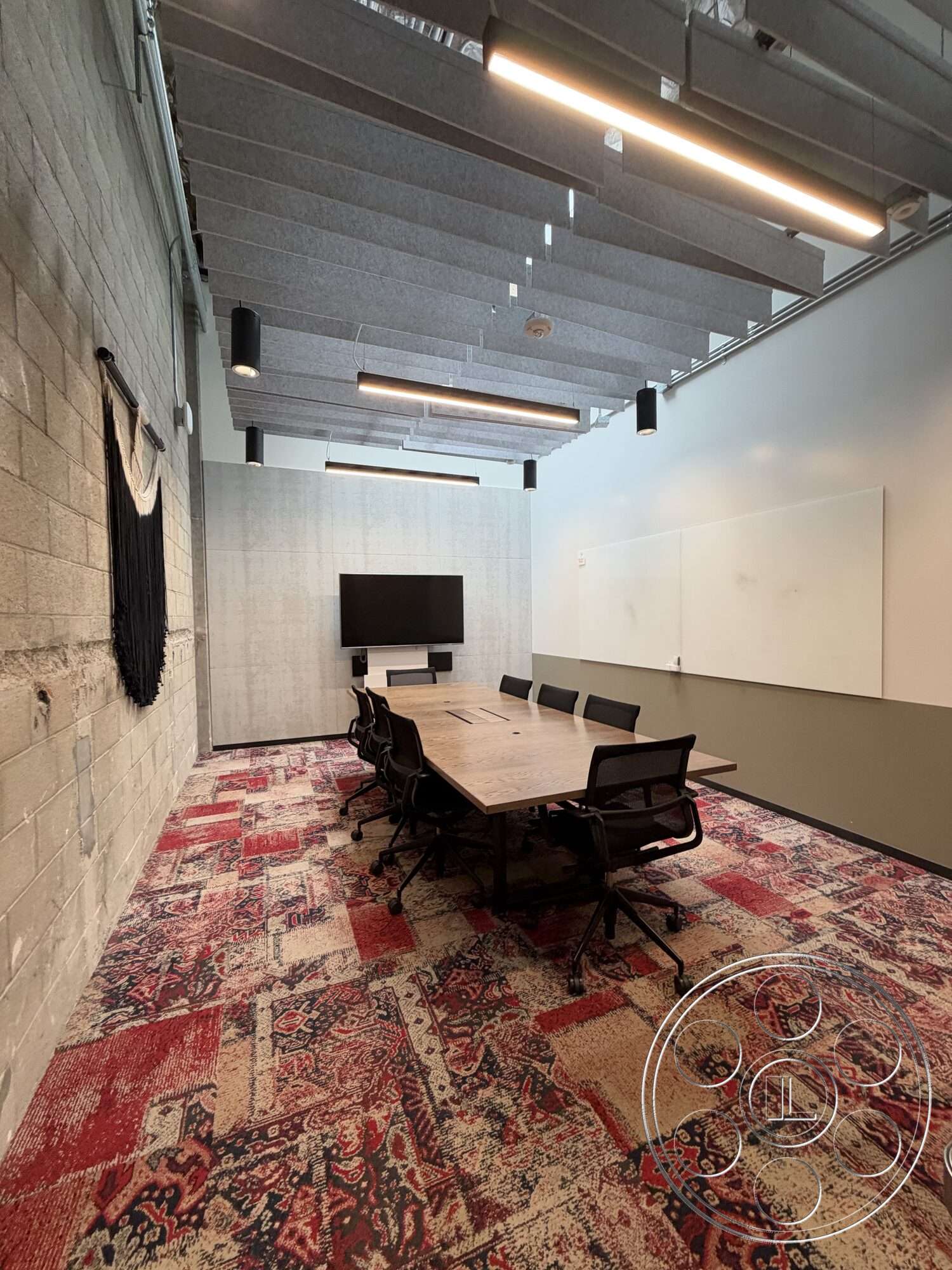 Office 130 - concrete block walls, industrial style, pendant lighting fixtures, acoustic ceiling panels, textured carpet flooring, wood conference table, whiteboard wall, black mesh office chairs, modern meeting room, wall-mounted flat-screen display, plaster finish walls