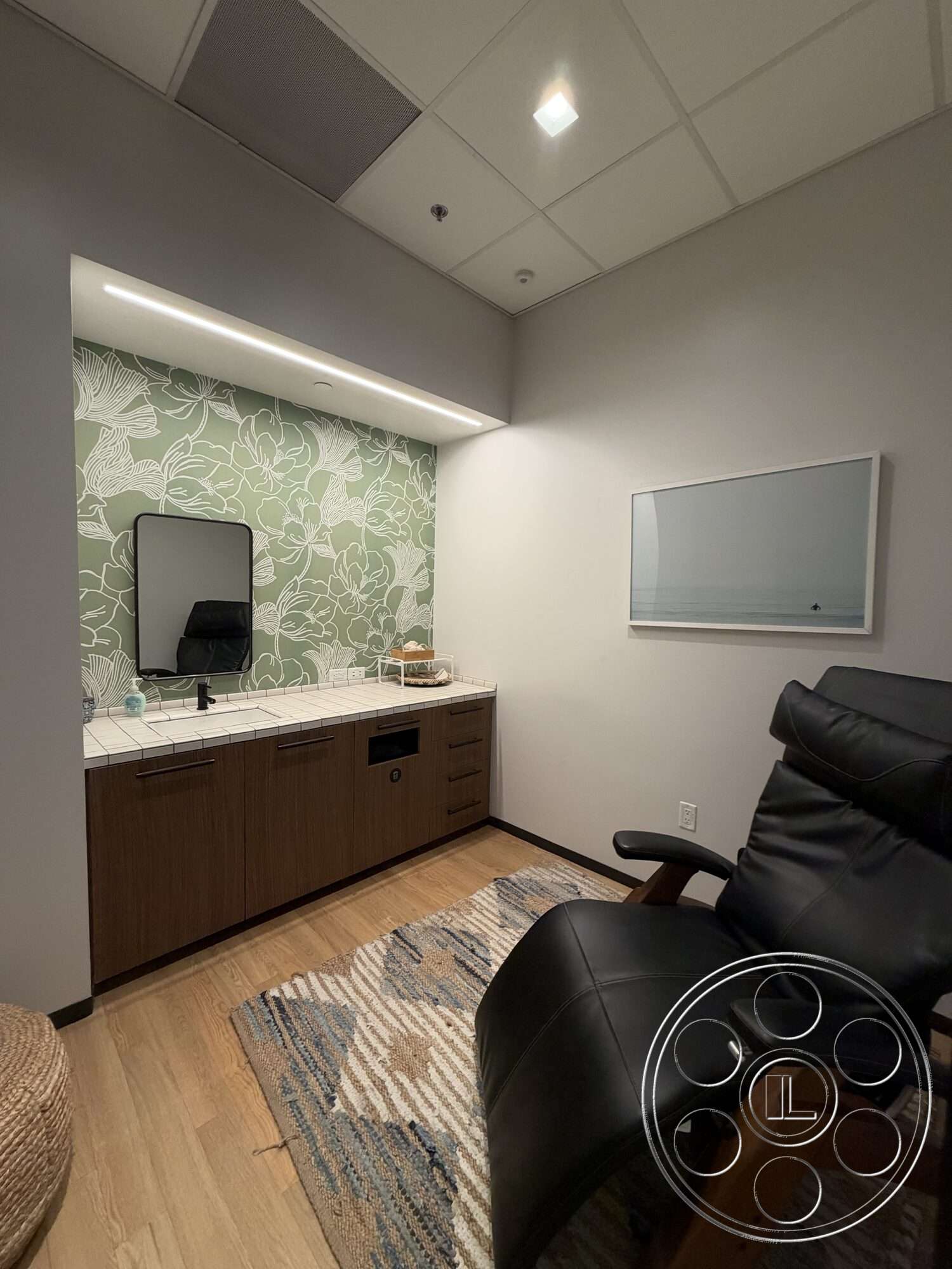 Office 130 - contemporary style, hardwood flooring, wood cabinetry, area rug, modern design elements, green floral wallpaper, mirrored wall, soft lighting fixtures, tile countertop, black leather recliner