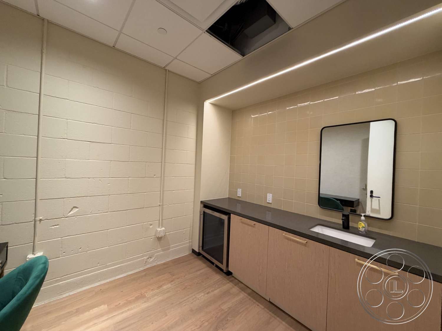 Office 130 - minimalist design, light wood cabinetry, dark stone countertop, laminate wood flooring, LED strip lighting, exposed concrete block walls, light beige tile backsplash, rectangular vanity mirror, modern interior space