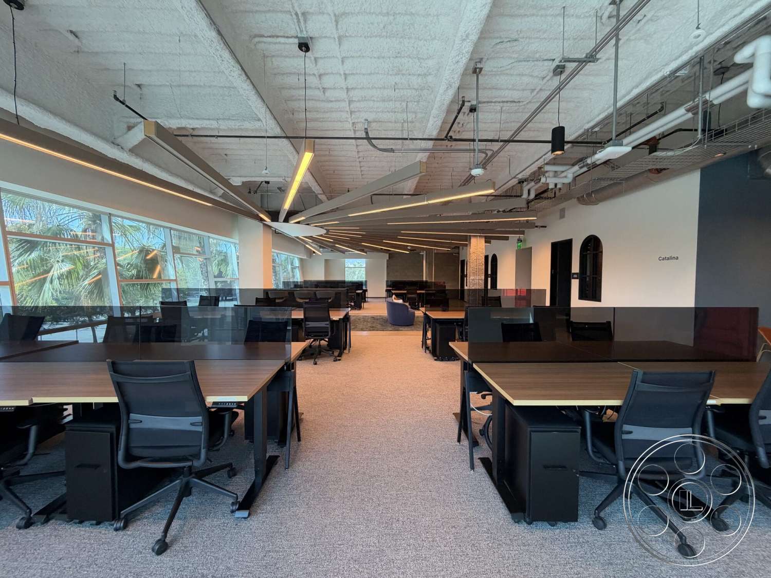 Office 130 - floor-to-ceiling windows, exposed concrete ceiling, gray carpet flooring, recessed ceiling lights, open office layout, modern industrial design, wooden office desks, black ergonomic office chairs, collaborative workspace area, LED lighting strips, glass partition screens, acoustic panel wall
