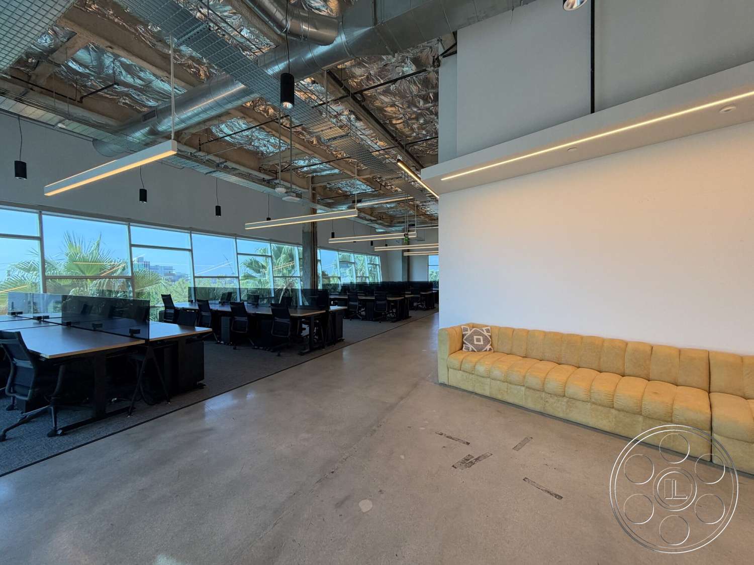 Office 130 - minimalist design, contemporary furniture, polished concrete flooring, large floor-to-ceiling windows, black office chairs, open office layout, track lighting fixtures, industrial-style decor, yellow upholstered sofa, suspended ceiling with exposed ductwork, glass desk dividers
