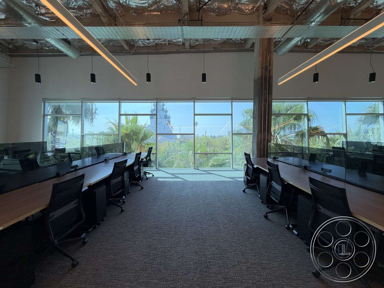 Office 130 - floor-to-ceiling windows, glass partition walls, interior office space, carpet office flooring, exposed concrete columns, open workspace layout, black ergonomic office chairs, high ceilings with exposed ductwork, wooden conference tables, modern LED pendant lighting, urban view with palm trees