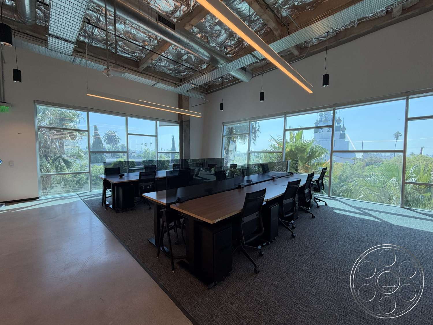 Office 130 - concrete flooring, city view, modern workspace, floor-to-ceiling windows, glass partition walls, carpet office flooring, exposed ductwork ceiling, urban office setting, open-plan office layout, linear LED ceiling lights, wood conference table, mesh office chairs, potted palm plants