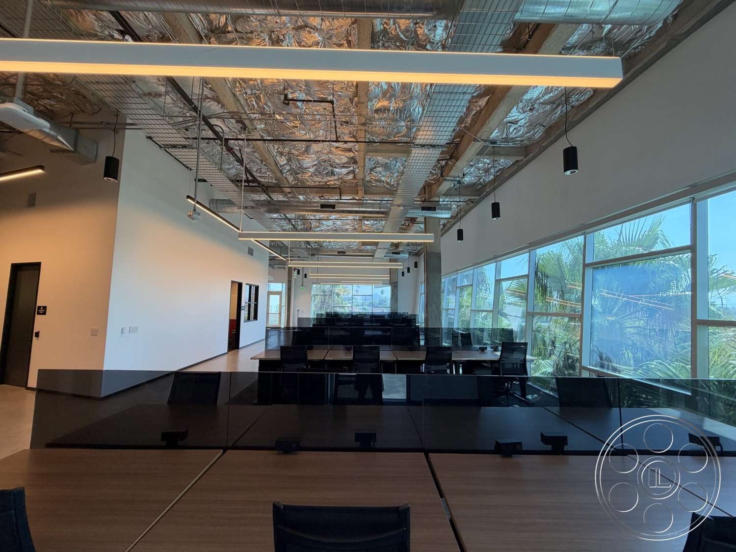Office 130 - floor-to-ceiling windows, exposed ductwork, black office chairs, palm tree view, open office layout, glass partition walls, linear LED ceiling lights, concrete accent wall, hardwood conference table, metal ceiling tiles