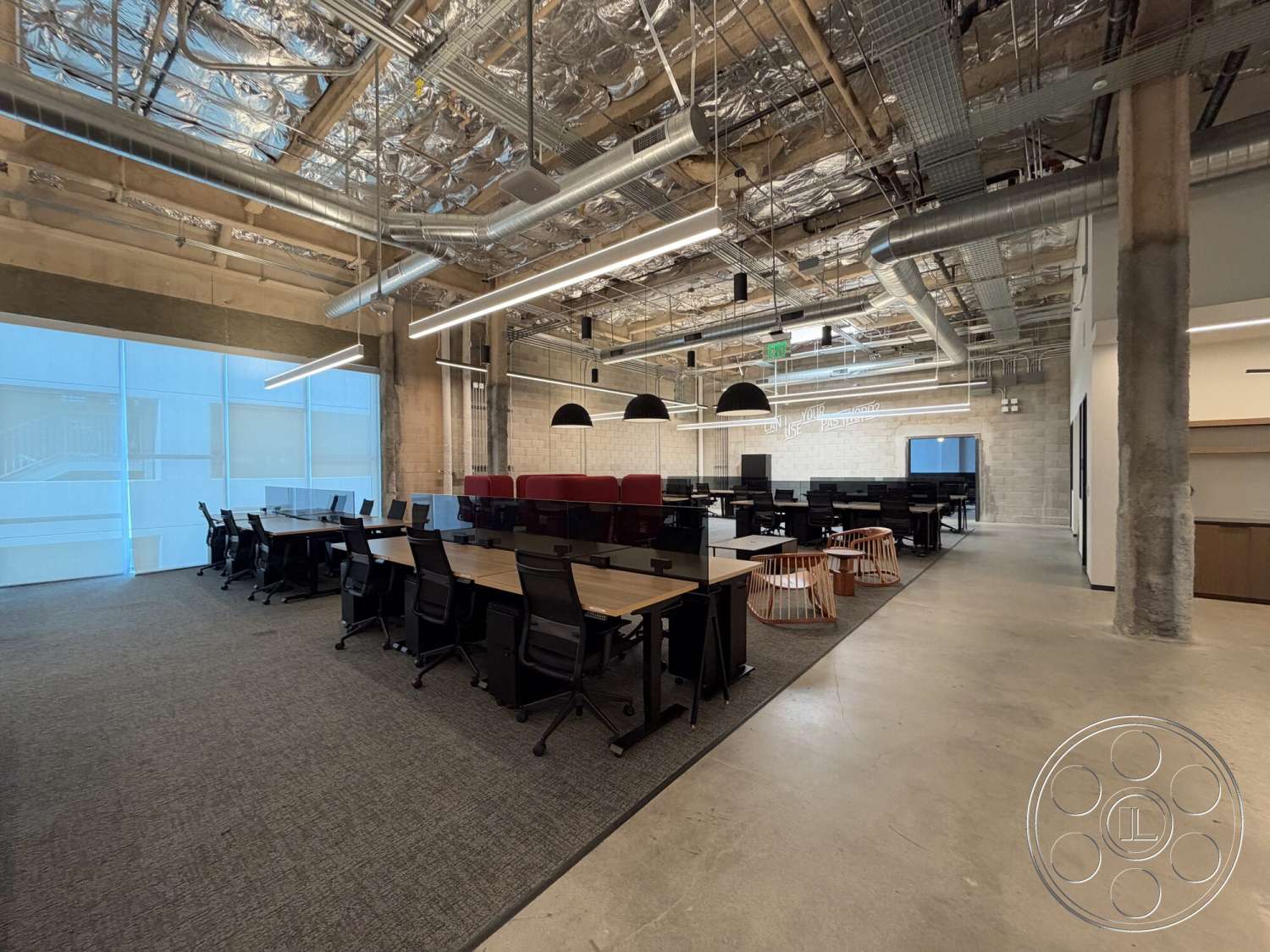 Office 130 - polished concrete flooring, exposed concrete walls, linear LED lighting, open office layout, glass partition walls, urban office environment, textured acoustic ceiling tiles, industrial pendant lighting, black ergonomic office chairs, neutral carpet tiles, steel ductwork, floating ceiling with metallic grid, rectangular wooden conference tables, collaborative seating area with wooden stools