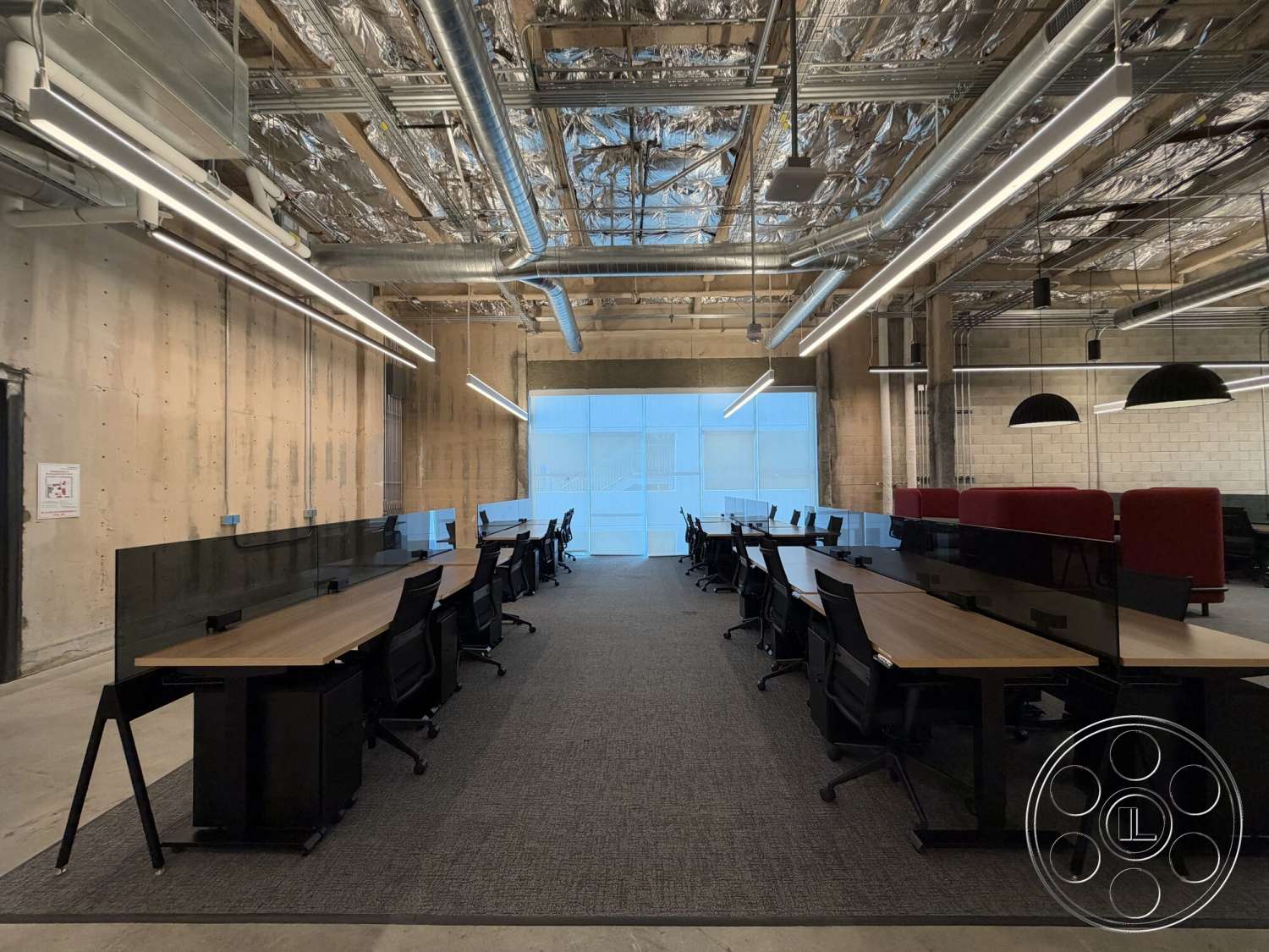 Office 130 - exposed concrete walls, suspended ceiling, black office chairs, open plan layout, carpet office flooring, metal ceiling beams, glass partition desks, linear LED light fixtures, wooden workspace surfaces, industrial office environment