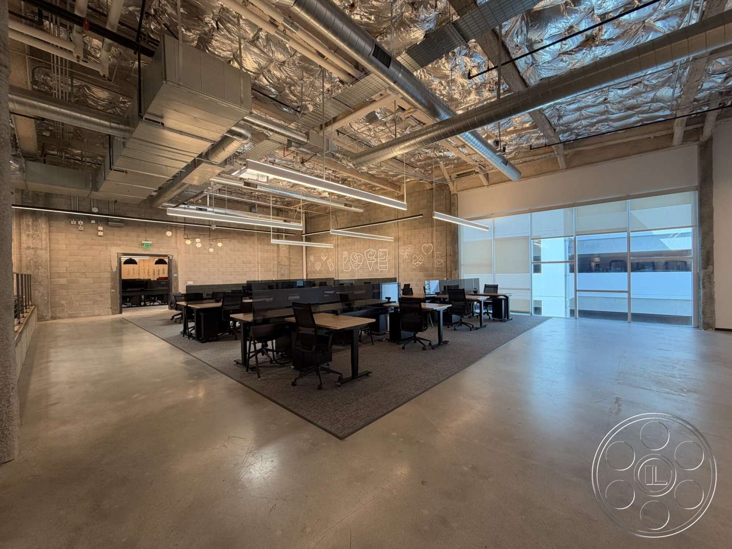 Office 130 - high ceilings, open floor plan, concrete flooring, exposed concrete walls, glass wall partitions, ergonomic office chairs, linear LED ceiling lights, industrial-style office space, gray carpet tiles, black office desks, drop ceiling with metal tiles, modern workplace design, structured HVAC ducting
