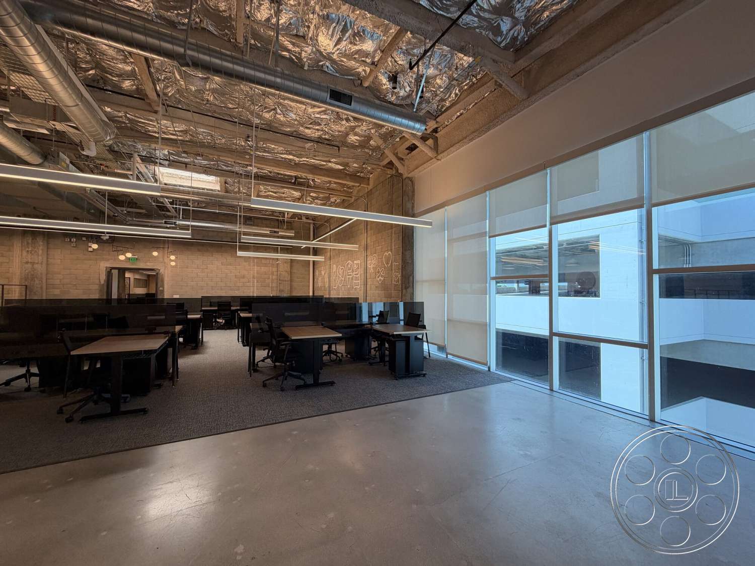Office 130 - polished concrete flooring, exposed concrete walls, large floor-to-ceiling windows, glass partition walls, interior office space, wooden office desks, drop ceiling with exposed ductwork, modern linear light fixtures, black workstation cubicles