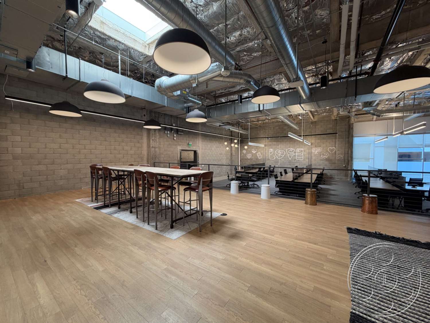 Office 130 - interior space, casual dining area, black metal railing, modern bar stools, wood laminate flooring, industrial hanging light fixtures, skylight overhead, exposed concrete block walls, open ceiling with ductwork, metal frame dining table