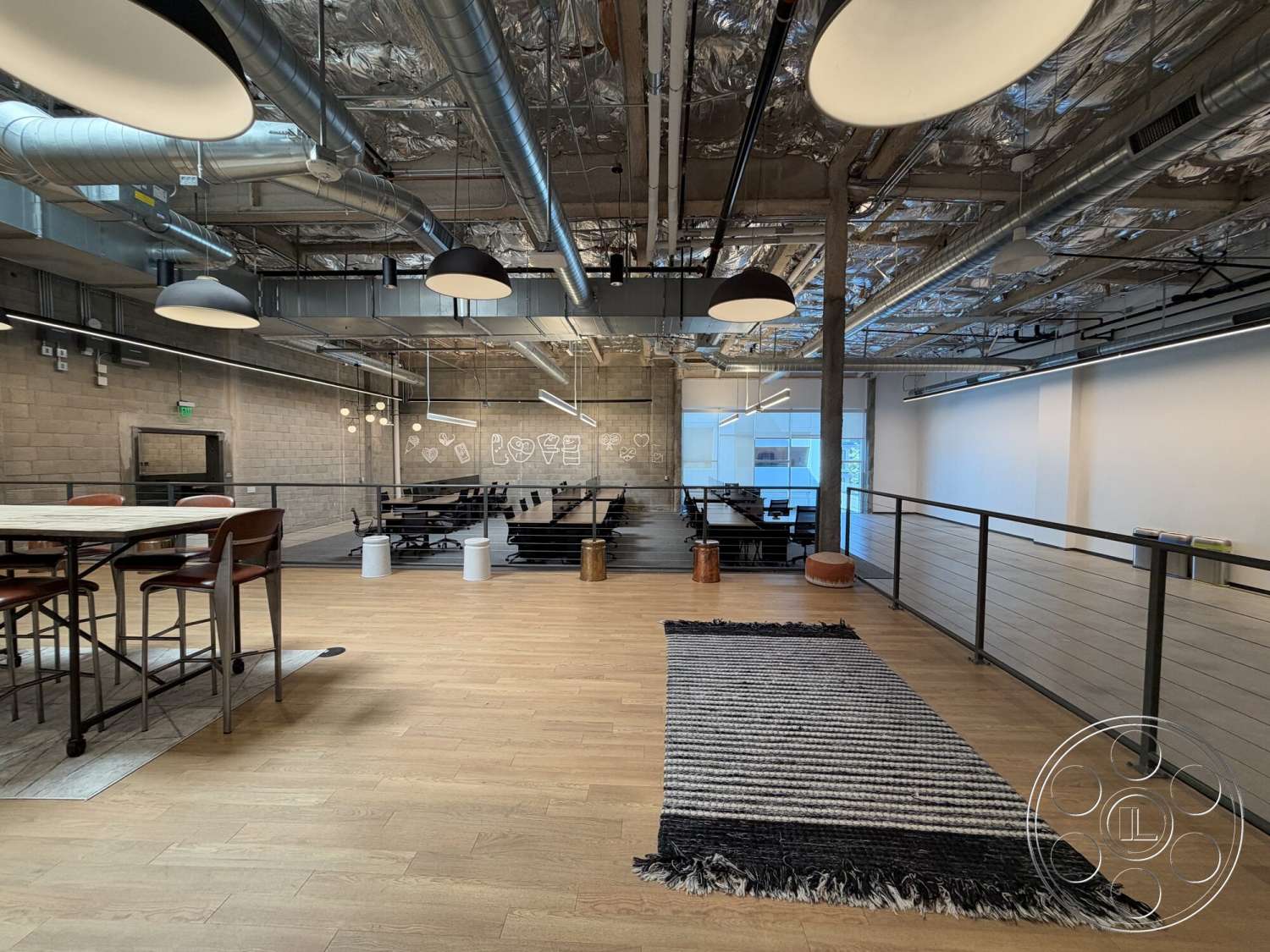 Office 130 - minimalist decor, open floor plan, exposed concrete walls, metal railing, collaborative workspace, striped area rug, black pendant lighting, glass wall partitions, polished hardwood flooring, industrial-style lighting, drop ceiling with exposed ductwork, wooden dining table with metal base, black chairs with metal frame