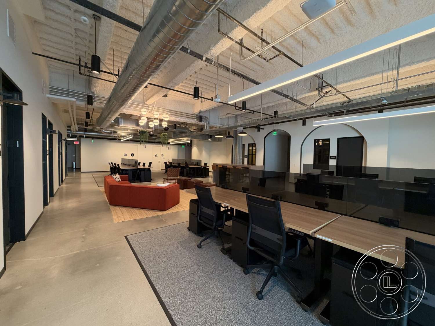 Office 130 - modern lighting fixtures, arched doorways, open office layout, white painted walls, industrial style architecture, exposed concrete flooring, wood conference table, textured acoustic ceiling, black glass desk partitions, black steel overhead ductwork, red upholstered seating area