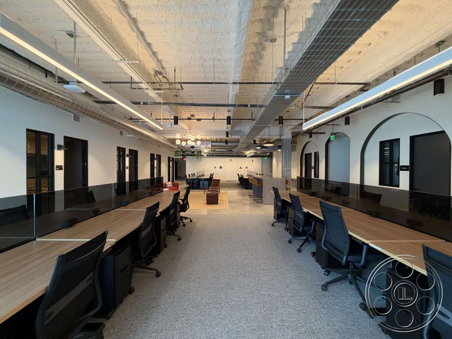 Office 130 - arched doorways, exposed concrete ceiling, metal ductwork, pendant lighting fixtures, open office layout, glass partition walls, modern office design, carpet office flooring, black ergonomic office chairs, collaborative workspace area, dark wood office furniture