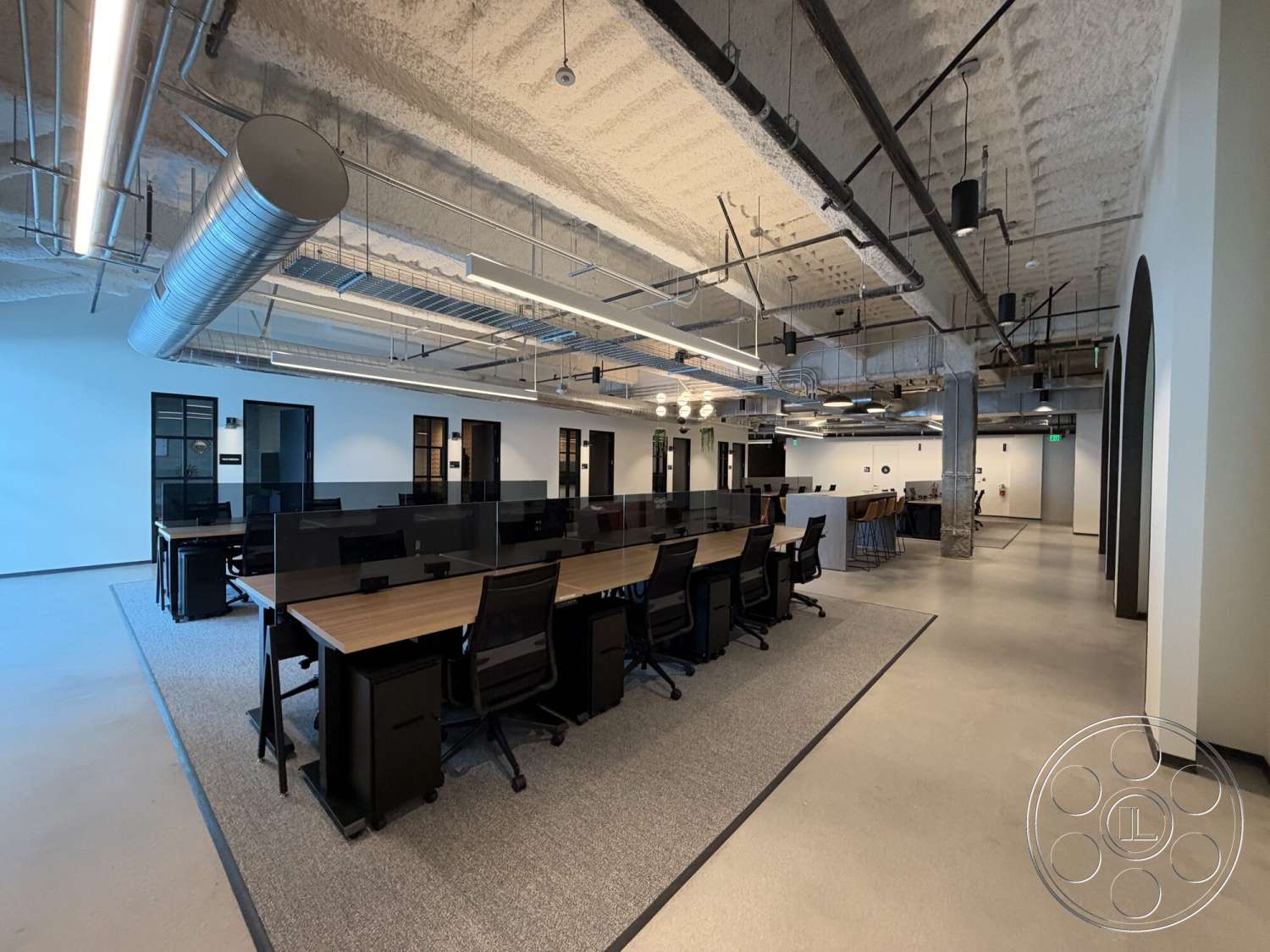 Office 130 - neutral color palette, concrete flooring, exposed concrete ceiling, metal ductwork, wooden desks, glass partition walls, modern office design, industrial-style lighting fixtures, interior workspace, black mesh office chairs, large open office area