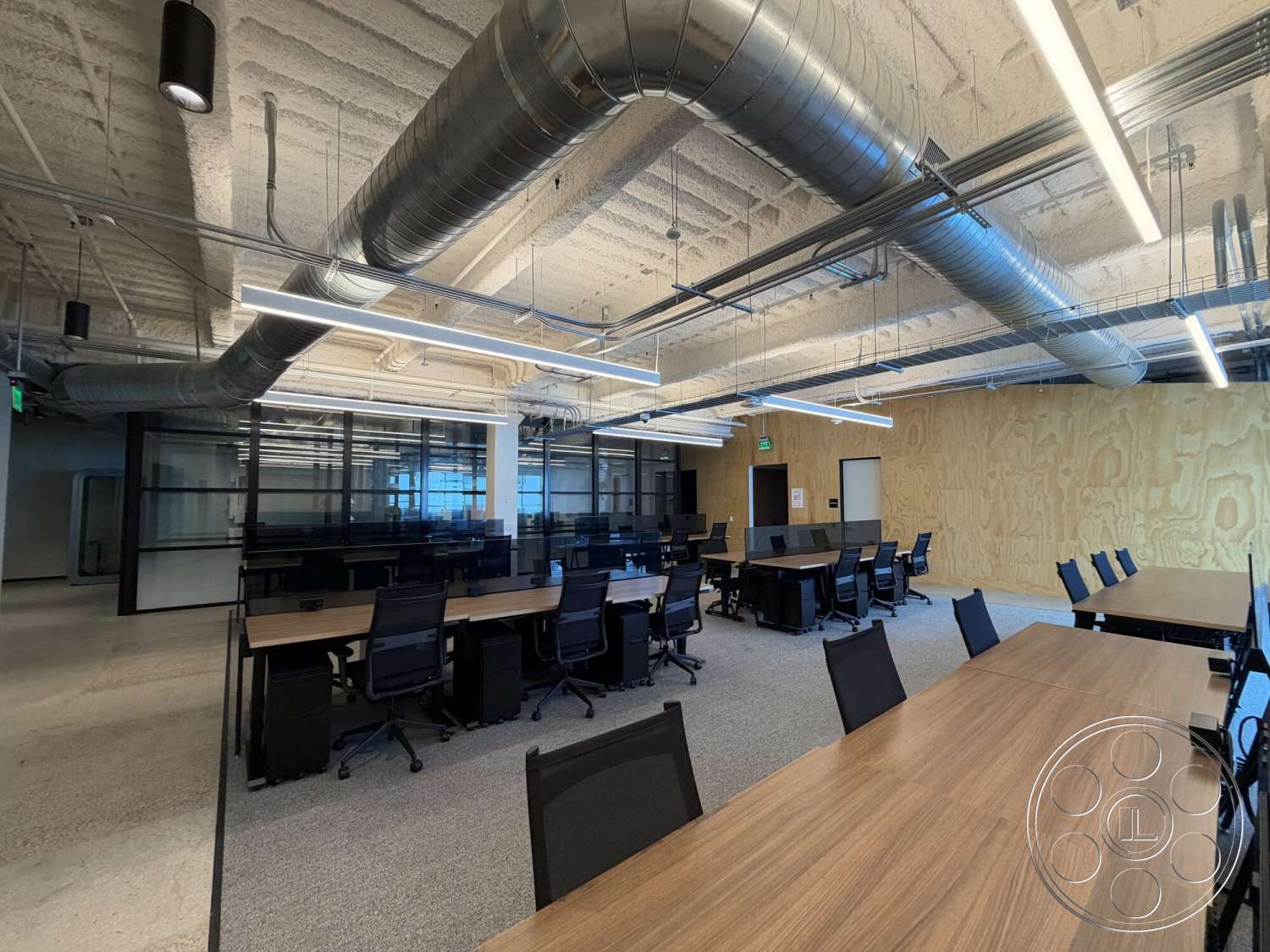 Office 130 - carpet flooring, open office layout, glass partition walls, exposed ductwork ceiling, commercial office space, fluorescent ceiling lights, rectangular workspace layout, plywood wall panels, black mesh office chairs, laminate office desks