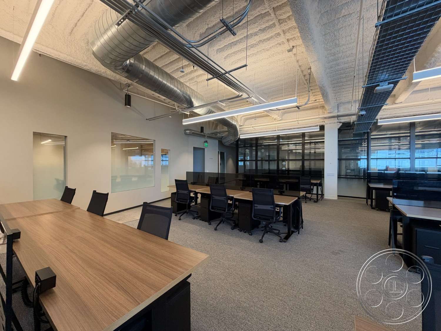 Office 130 - open floor plan, concrete flooring, large glass windows, textured wall finish, industrial style, collaborative workspace, exposed ductwork, acoustic ceiling tiles, glass partition walls, steel frame support, modern office design, black mesh office chairs, wooden conference tables, LED linear lighting