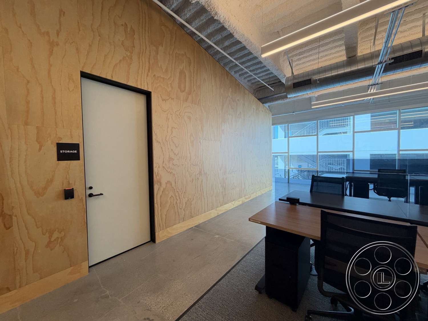 Office 130 - glass partition, modern workspace, smooth concrete flooring, open office layout, white painted door, textured ceiling finish, industrial-style lighting, black door hardware, plywood wall paneling