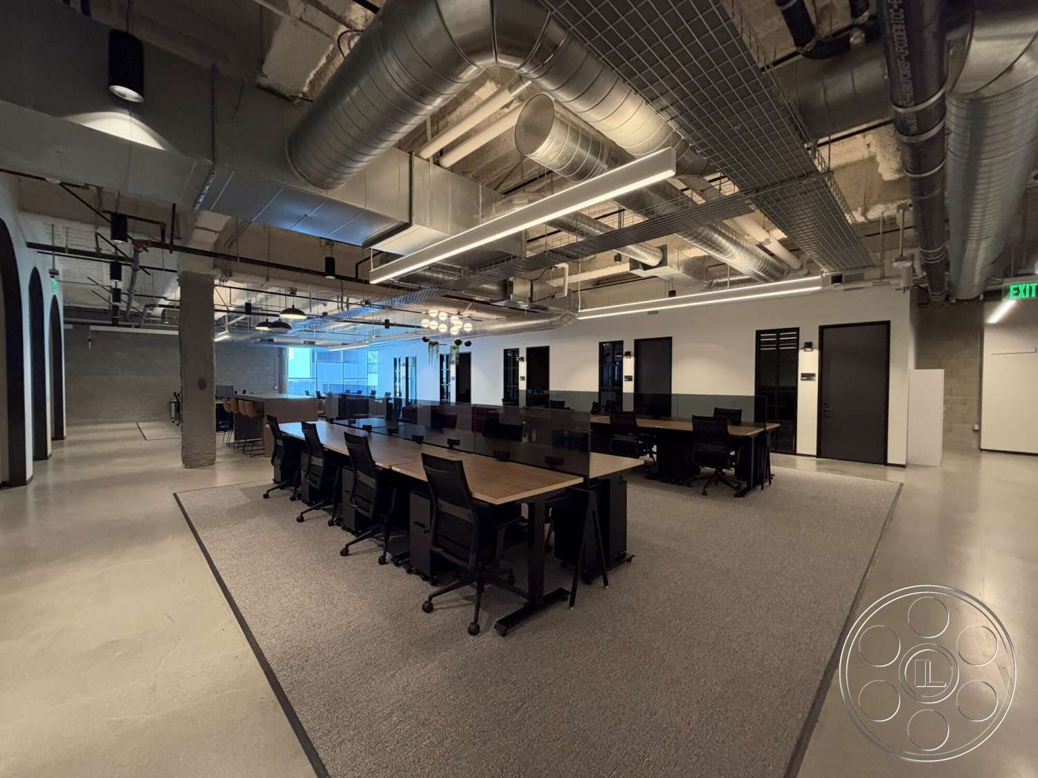 Office 130 - polished concrete flooring, exposed concrete walls, black office chairs, open plan layout, glass partition walls, interior office space, industrial style lighting fixtures, metal ductwork ceiling, drop ceiling lights, wood laminate desks, acoustic carpet tiles