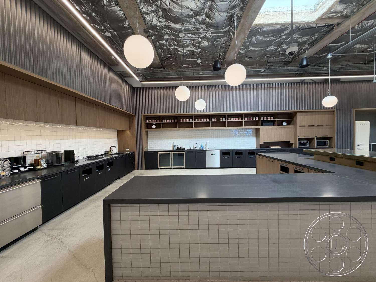 Office 130 - recessed lighting, stainless steel appliances, concrete flooring, black cabinetry, exposed ceiling beams, pendant lighting fixtures, modern kitchen design, white subway tile backsplash, open floor layout, kitchen island with overhang, wood grain kitchen cabinets, bulkhead ceiling, shelving units with decorative items