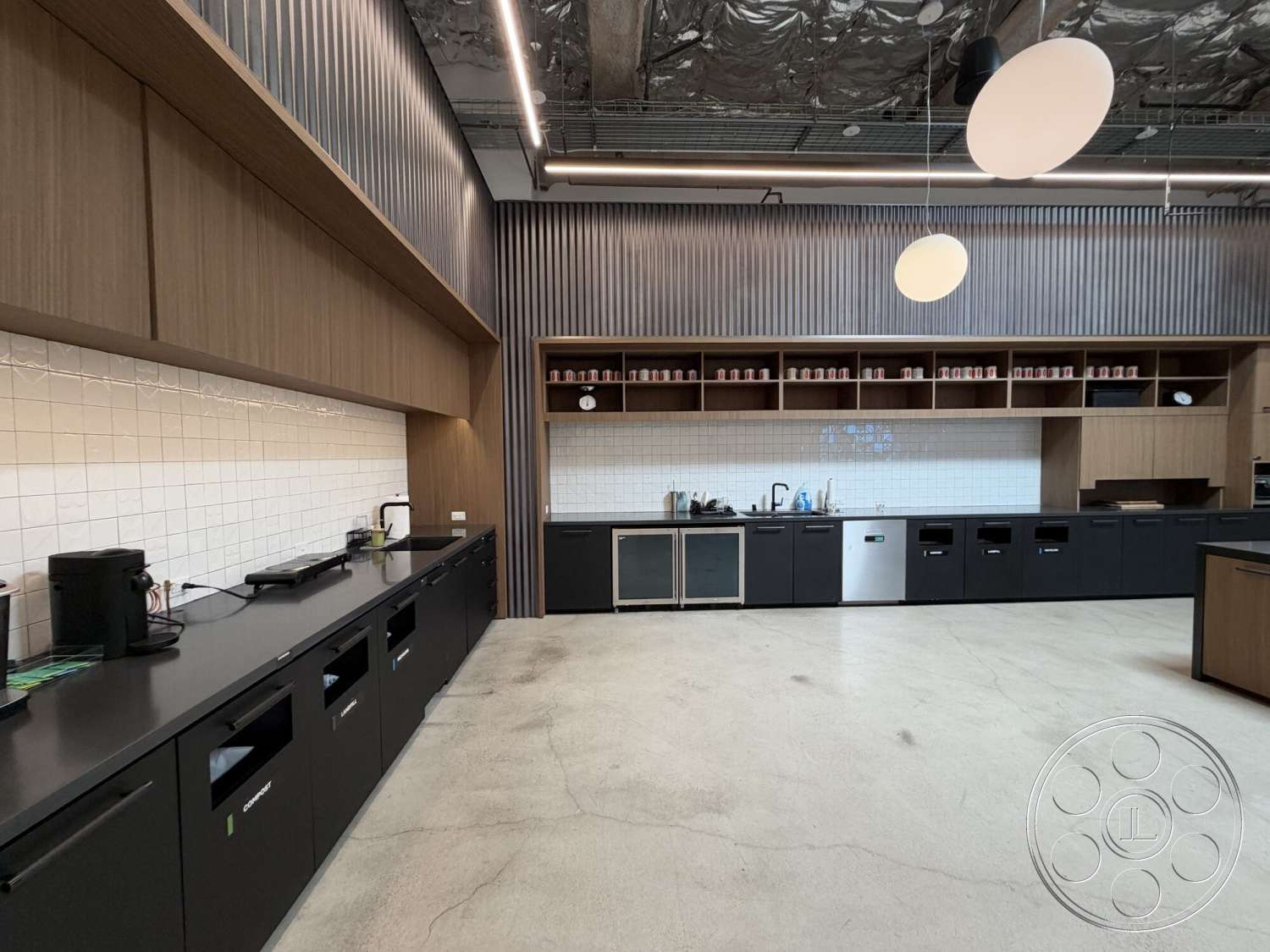Office 130 - wood cabinetry, open shelving, concrete flooring, linear pendant lighting, horizontal wood paneling, steel appliances, white tile backsplash, black kitchen counters, slab concrete walls