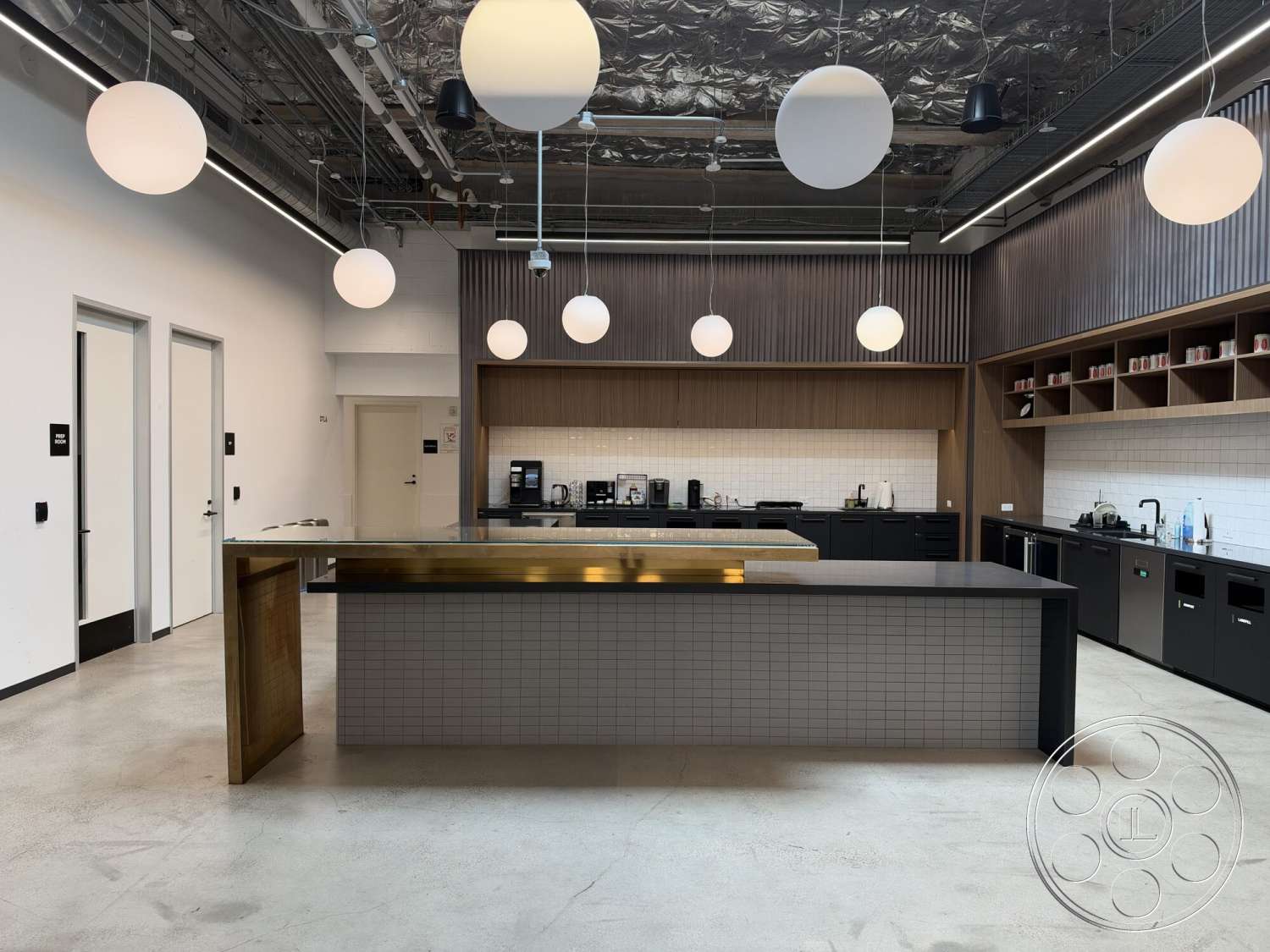 Office 130 - minimalist aesthetic, concrete flooring, sliding glass doors, exposed ductwork, linear pendant lighting, two-tone cabinetry, modern kitchen design, wooden kitchen cabinets, tile kitchen backsplash, open shelving units, panelled wall treatment, black kitchen countertops, brass kitchen island top