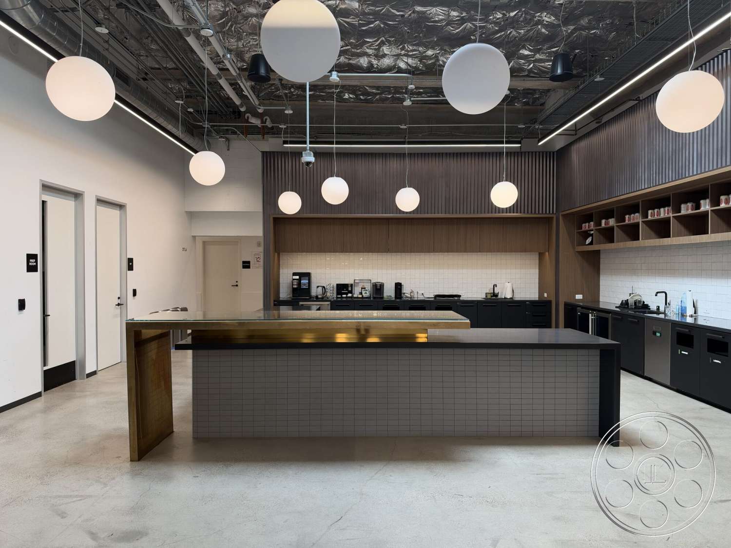 Office 130 - minimalist design, concrete flooring, open concept layout, recessed ceiling lighting, textured ceiling treatment, built-in kitchen appliances, white subway tile backsplash, modern industrial style, black tile kitchen countertops, metal bar counter with brass trim, wood cabinetry with dark finish, spherical pendant lights