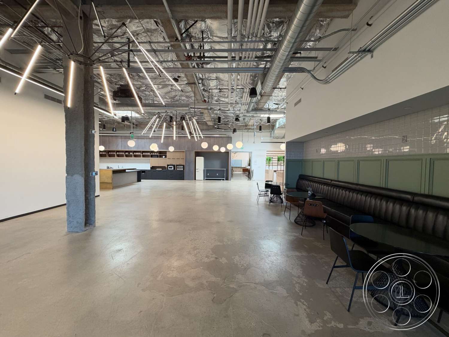 Office 130 - interior space, concrete walls, modern dining chairs, white subway tile backsplash, track lighting fixtures, exposed concrete flooring, industrial-style decor, metal ceiling beams, pendant light fixtures, dark wood kitchen cabinets, open kitchen area, black leather banquette seating, glass dining tables