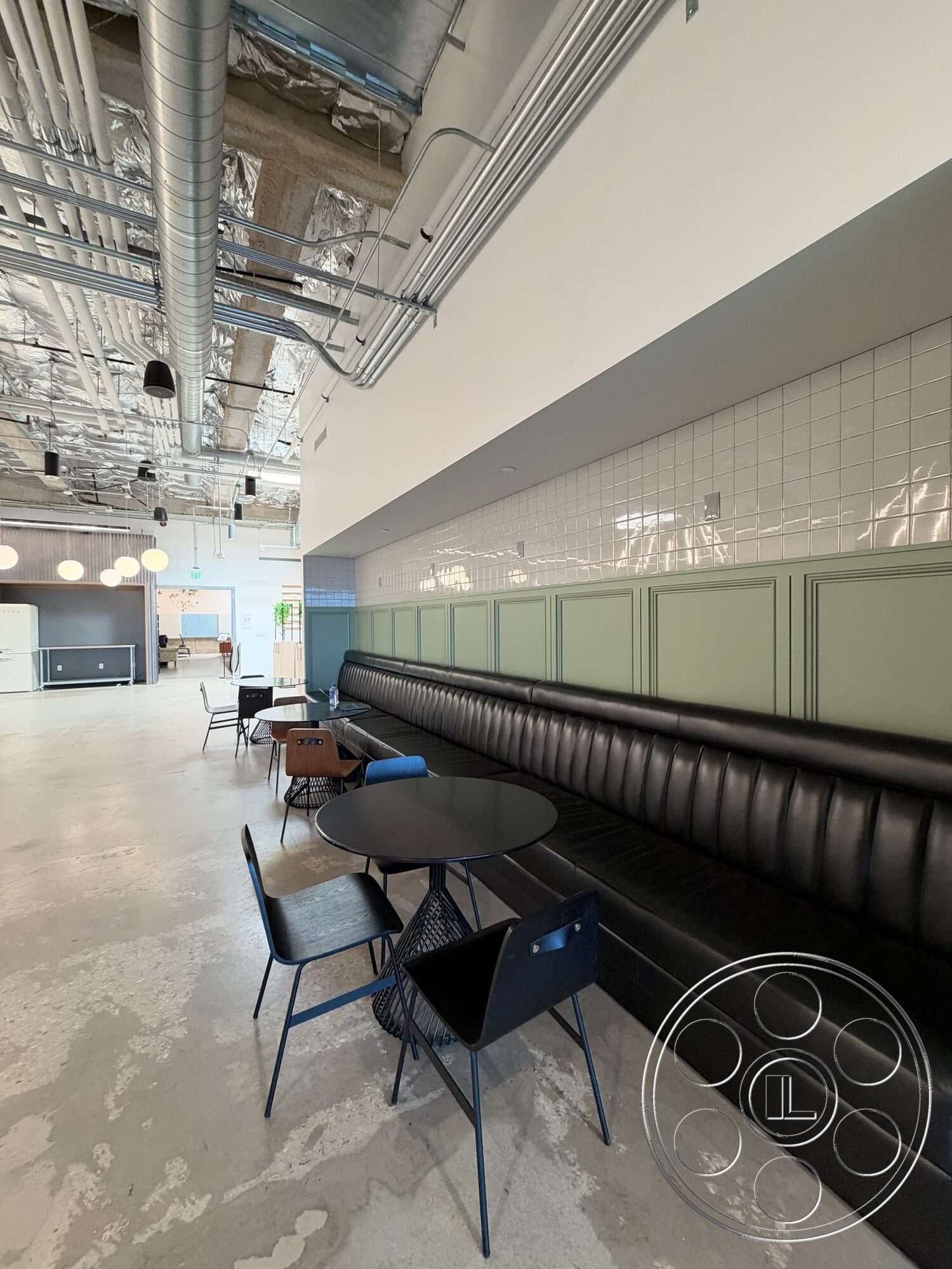 Office 130 - open floor plan, polished concrete flooring, modern interior design, black metal dining chairs, exposed ductwork ceiling, black leather banquette seating, green cabinetry with paneling, dark metal wire table, white subway tile wall, commercial space dining area