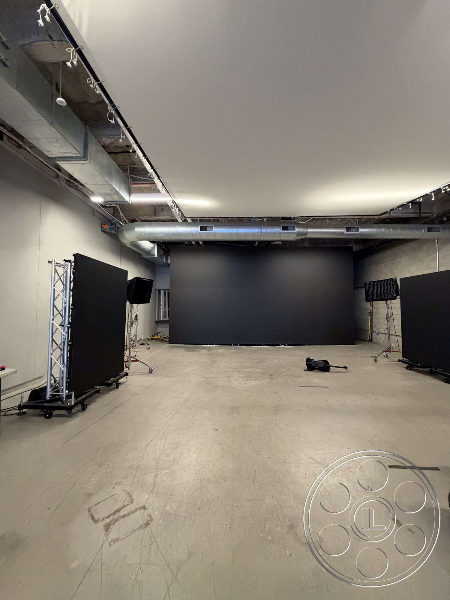 Office 130 - concrete floor, exposed concrete walls, industrial lighting, studio setup, ceiling-mounted ventilation ducts, black backdrop screen