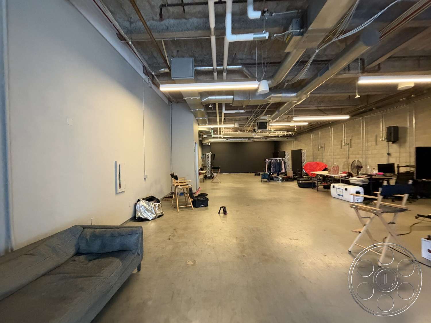 Office 130 - polished concrete flooring, exposed concrete walls, minimalist furniture design, track lighting fixtures, open layout interior, industrial ceiling with exposed ductwork, urban studio setting, warehouse-style space, black painted feature wall, flexible work area