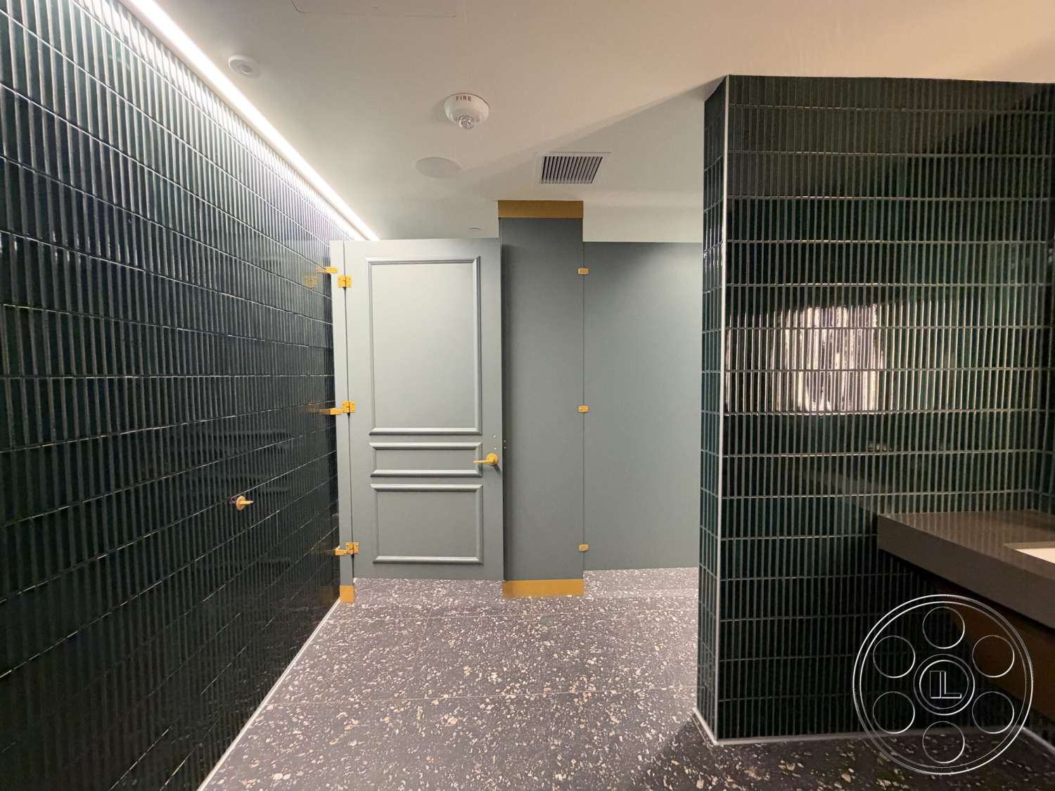 Office 130 - modern design, flush mount lighting, green glazed tile walls, gold hardware door, black speckled terrazzo flooring, dimensional wall treatment, framed mirror detail, accent wall design