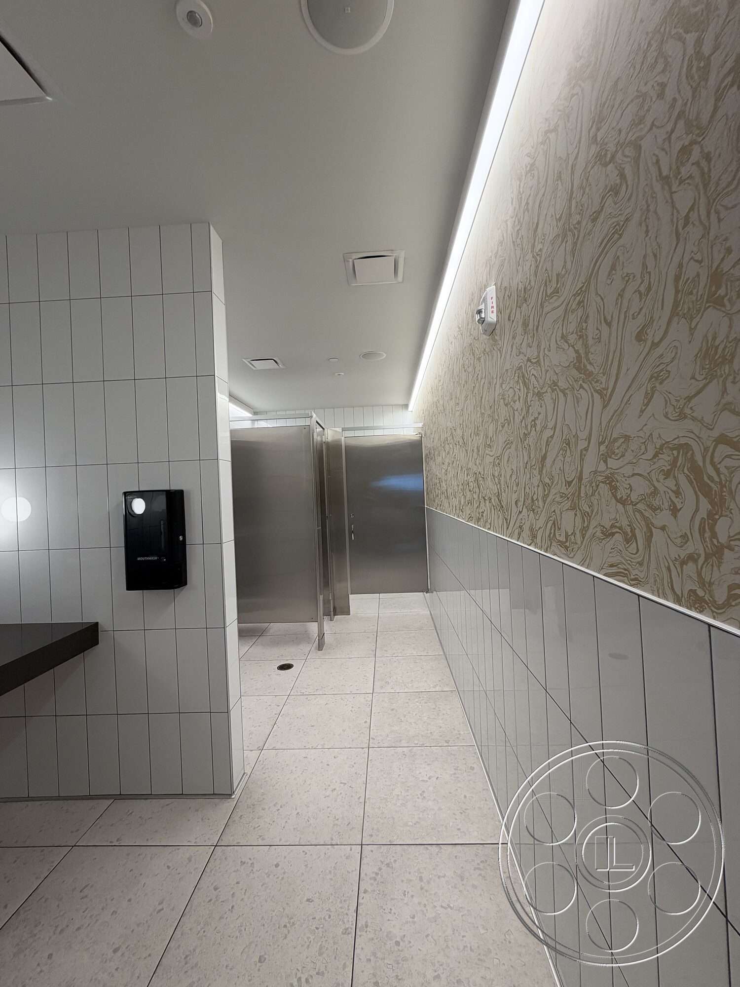 Office 130 - stainless steel fixtures, recessed ceiling lighting, interior restroom, metal partition walls, large format tile flooring, white ceramic tile walls, textured marble accent wall, grouted tile flooring, black solid surface countertop, modern flush ceiling vents