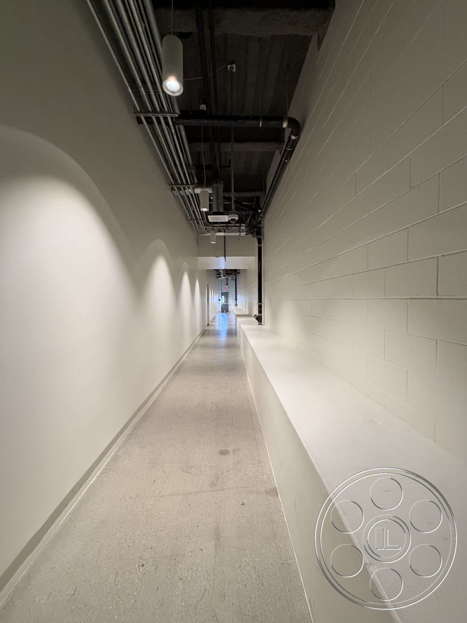 Office 130 - concrete flooring, industrial lighting fixtures, exposed ceiling, metal piping, linear layout, interior hallway, white painted walls, smooth wall surface